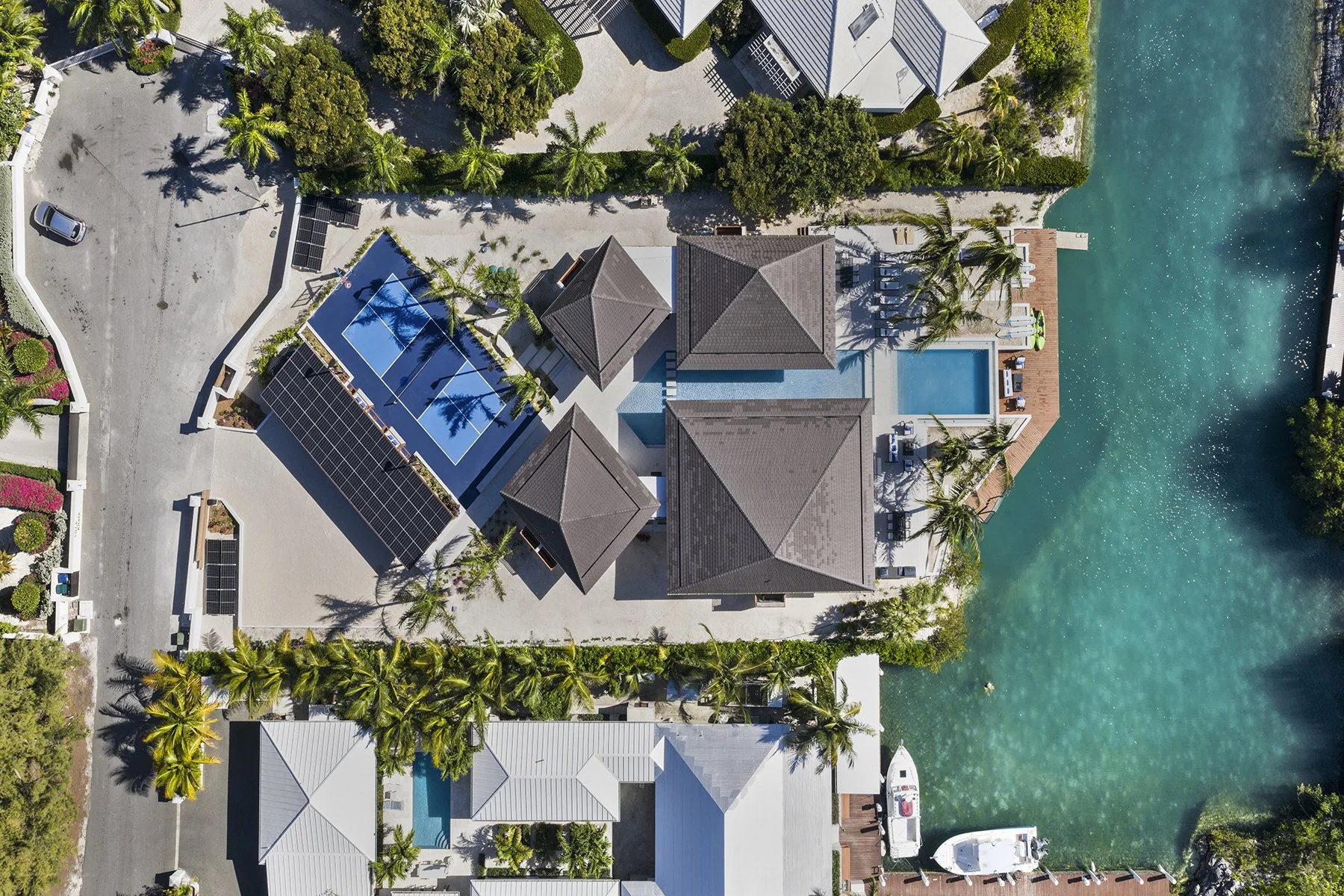Aerial view of a waterfront residential property with a swimming pool, tennis court, boats, and surrounding greenery.