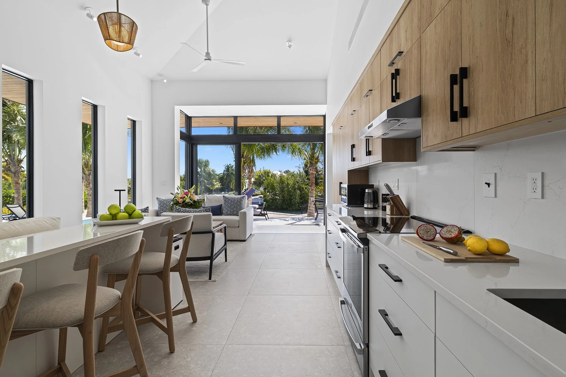 Modern kitchen and living room with large glass doors opening to outdoor patio with trees and palm trees