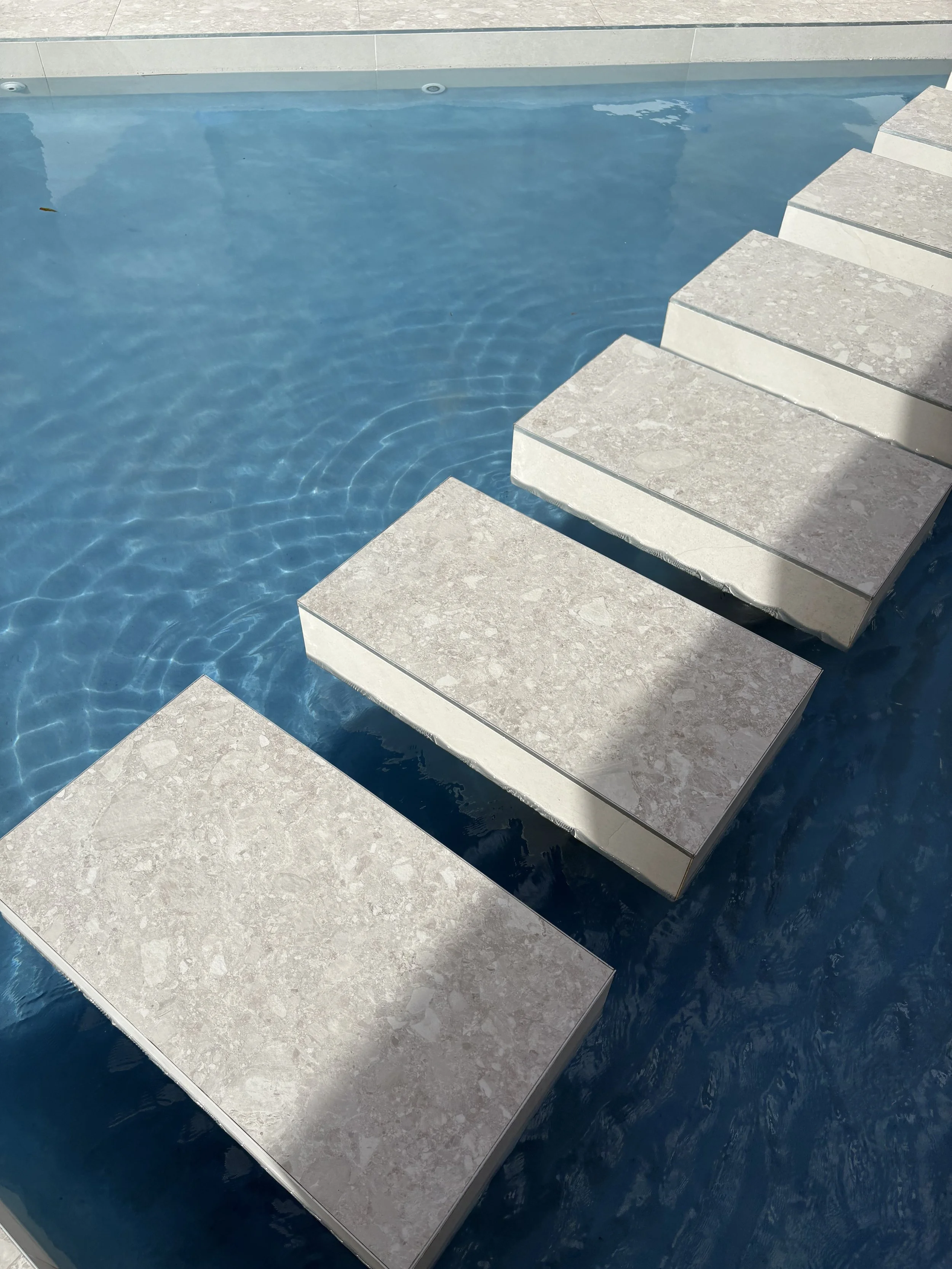 A swimming pool with steps and floating stone blocks.