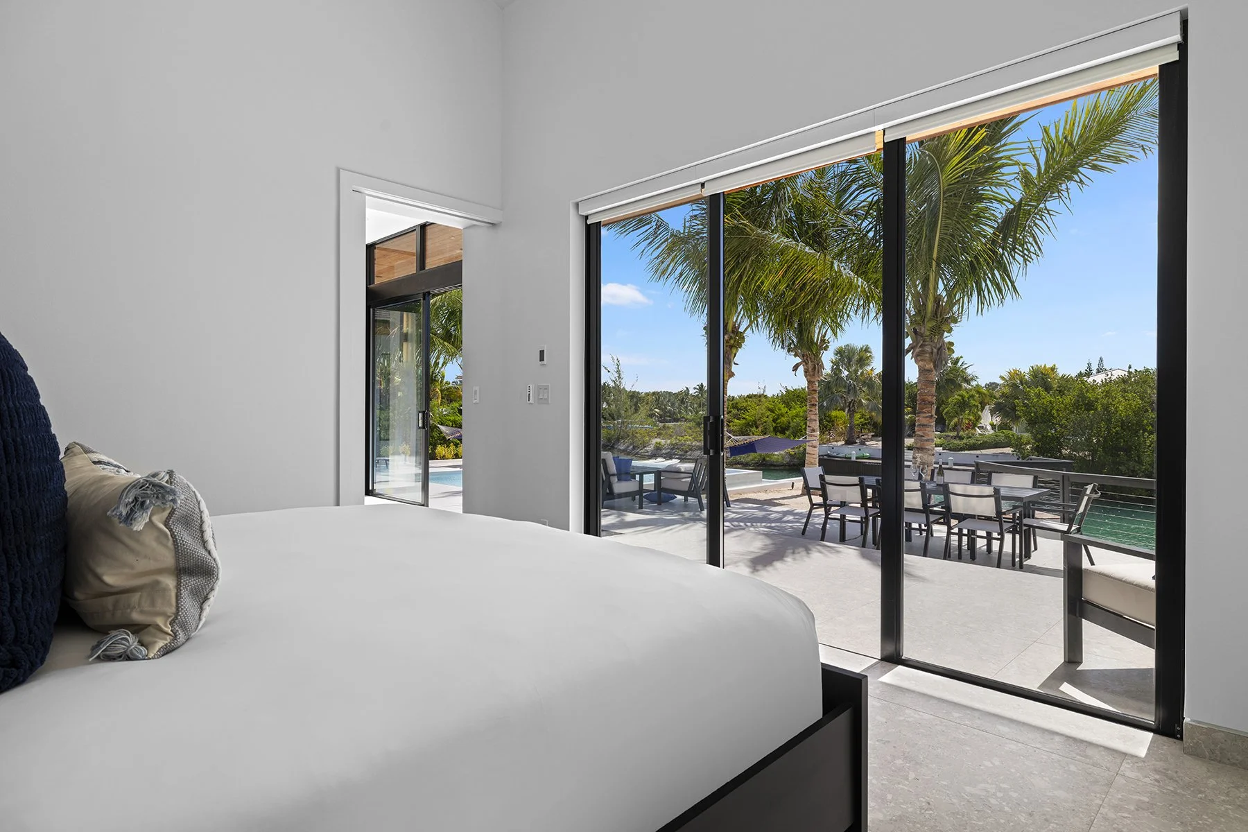 Bedroom with sliding glass doors opening to a patio with palm trees and outdoor seating