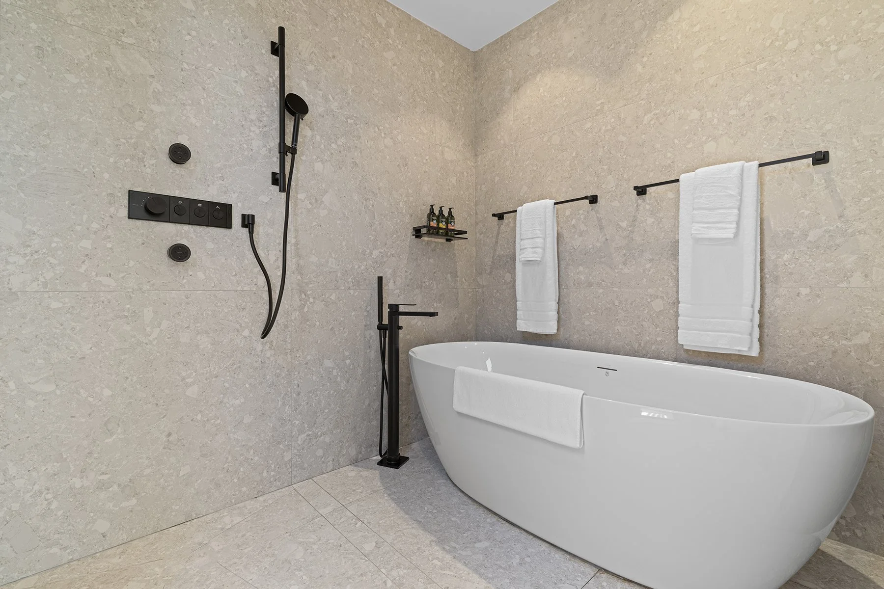 Modern bathroom with a freestanding bathtub, black shower fixtures, and white towels hanging on black rods.