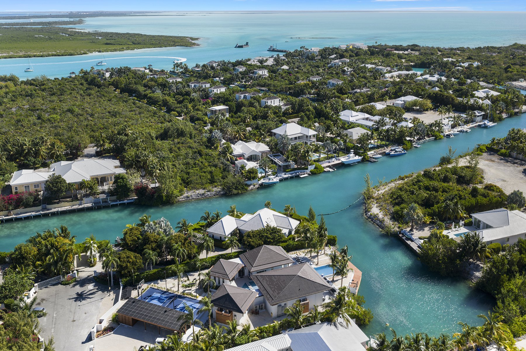 Aerial view of waterfront houses with boats along a canal in a tropical coastal area.