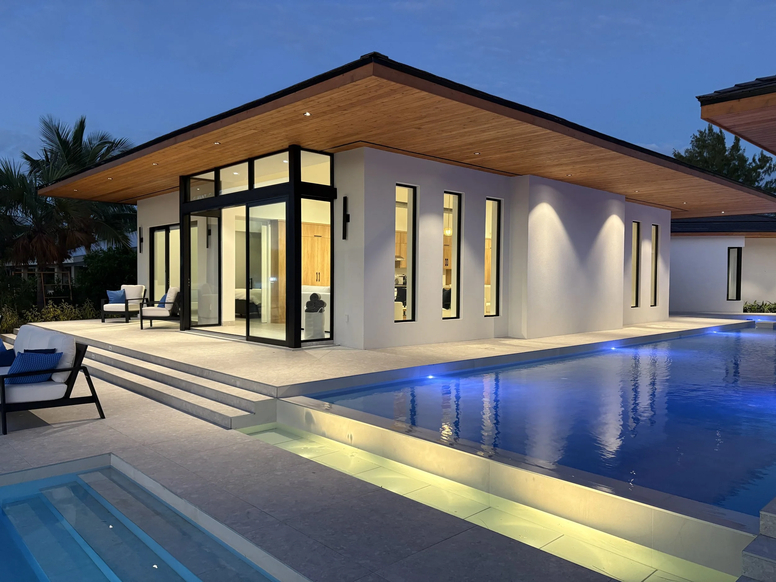 Modern house with large glass windows and a pool outside, illuminated at dusk.