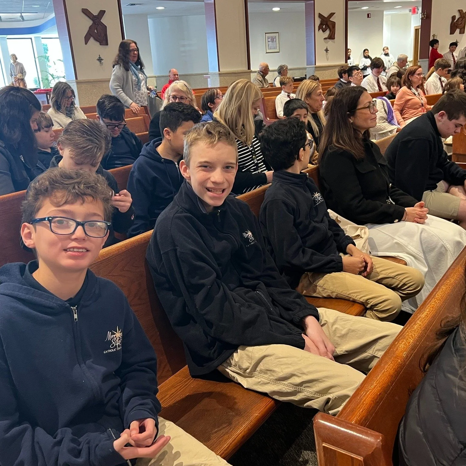 Group of students and adults seated in pews inside a church ready for a religious service.