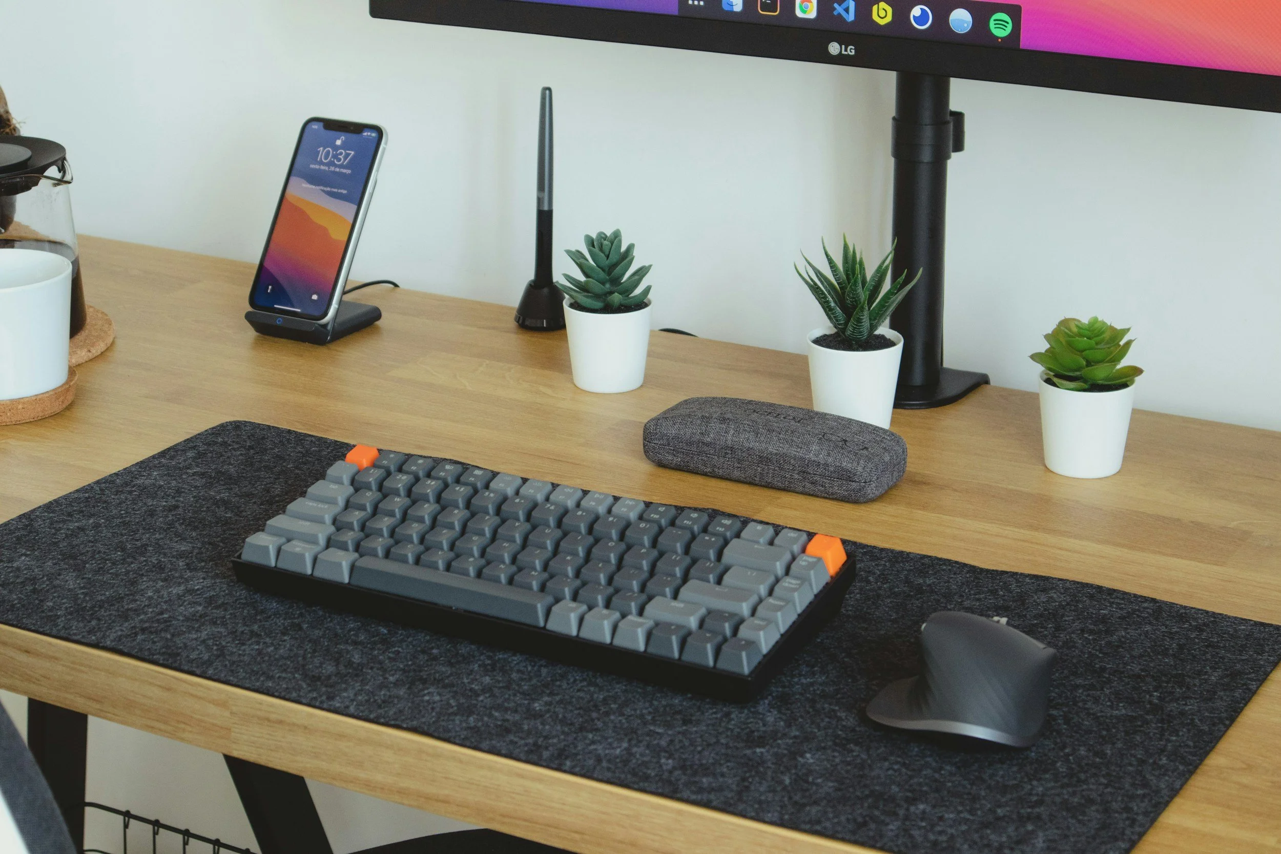 A gray computer keyboard on a desk next to a phone and plants.