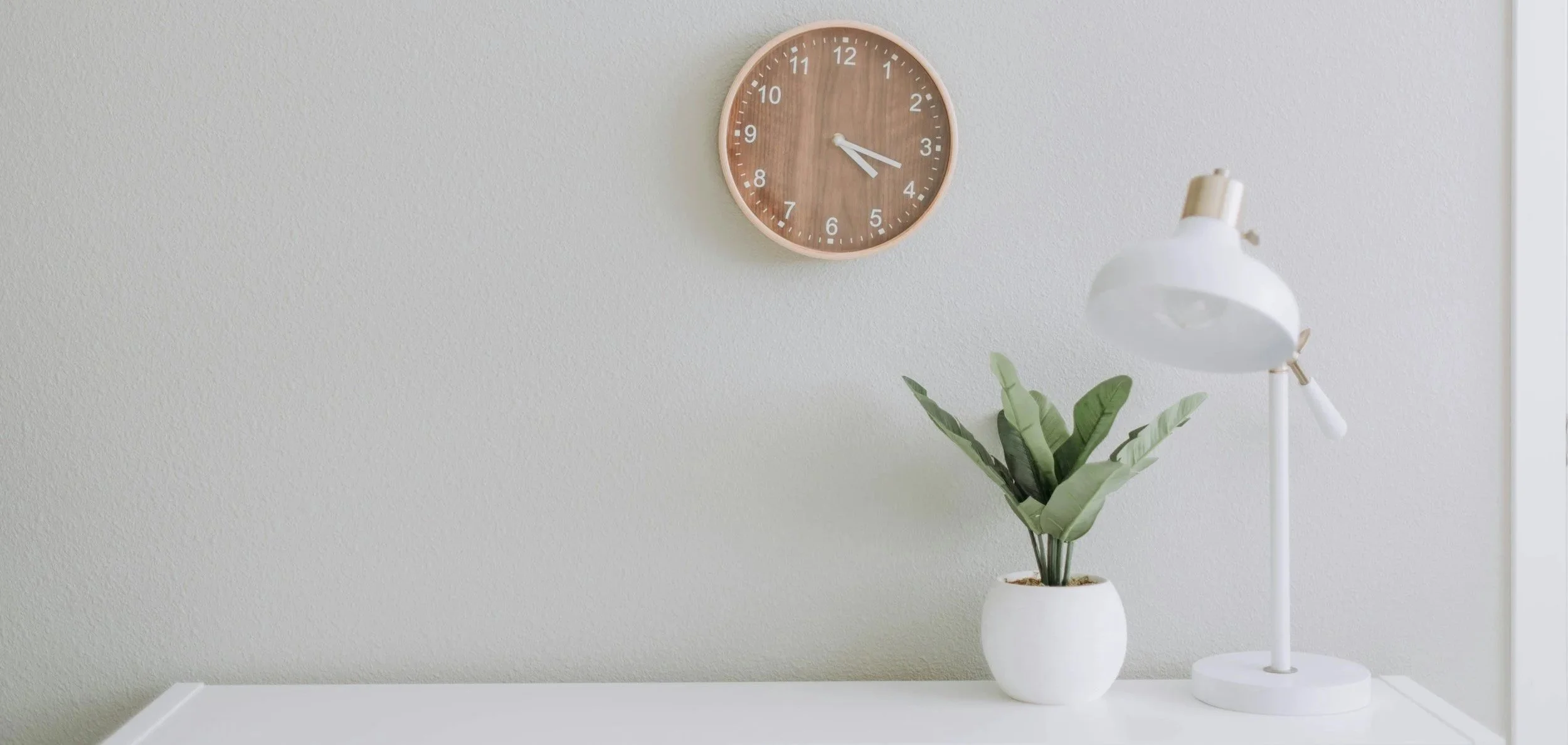 A clean office space with a plant, lamp and clock for decor.