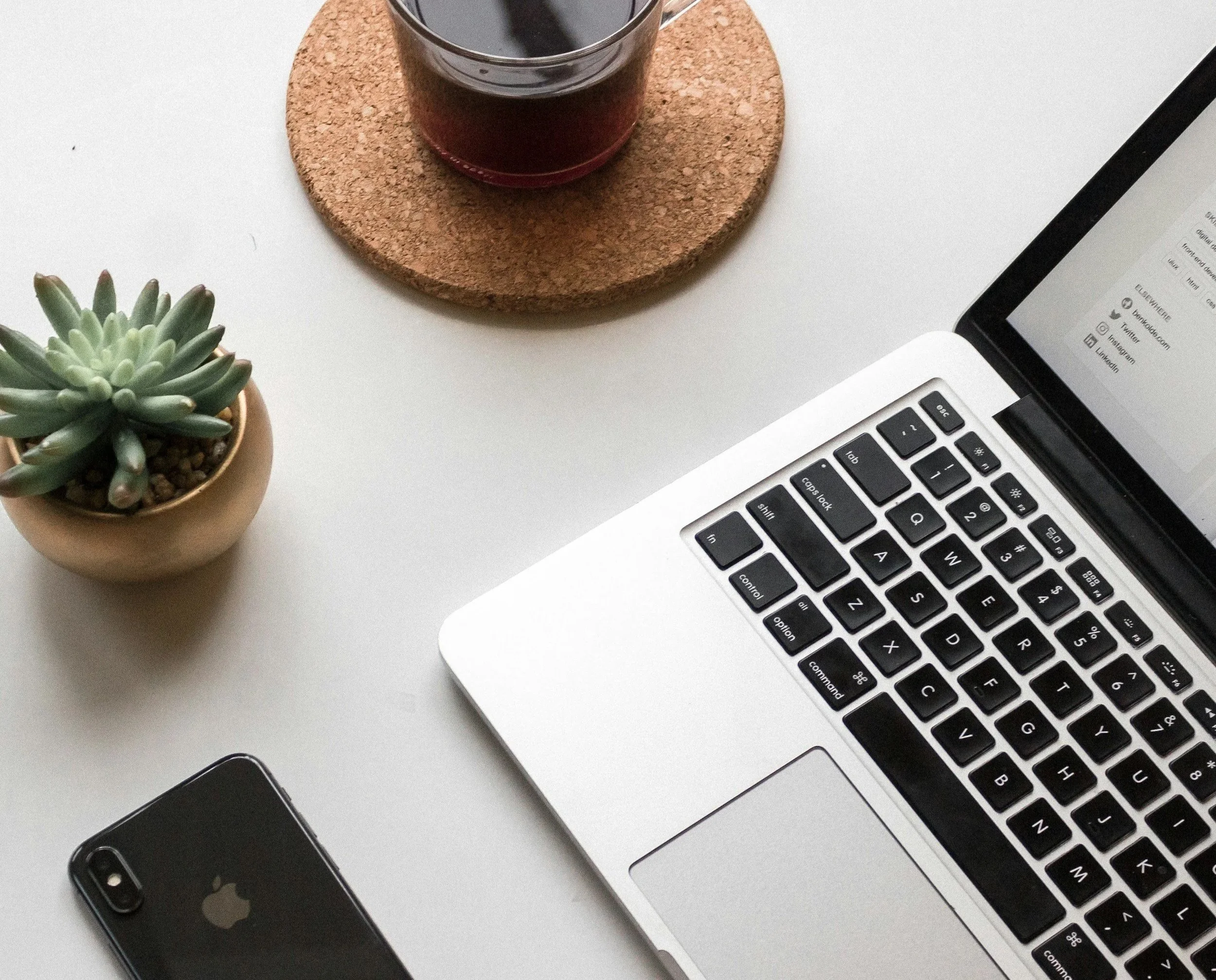 The edge of a computer, a coffee cup, a phone, and a plant are shown.