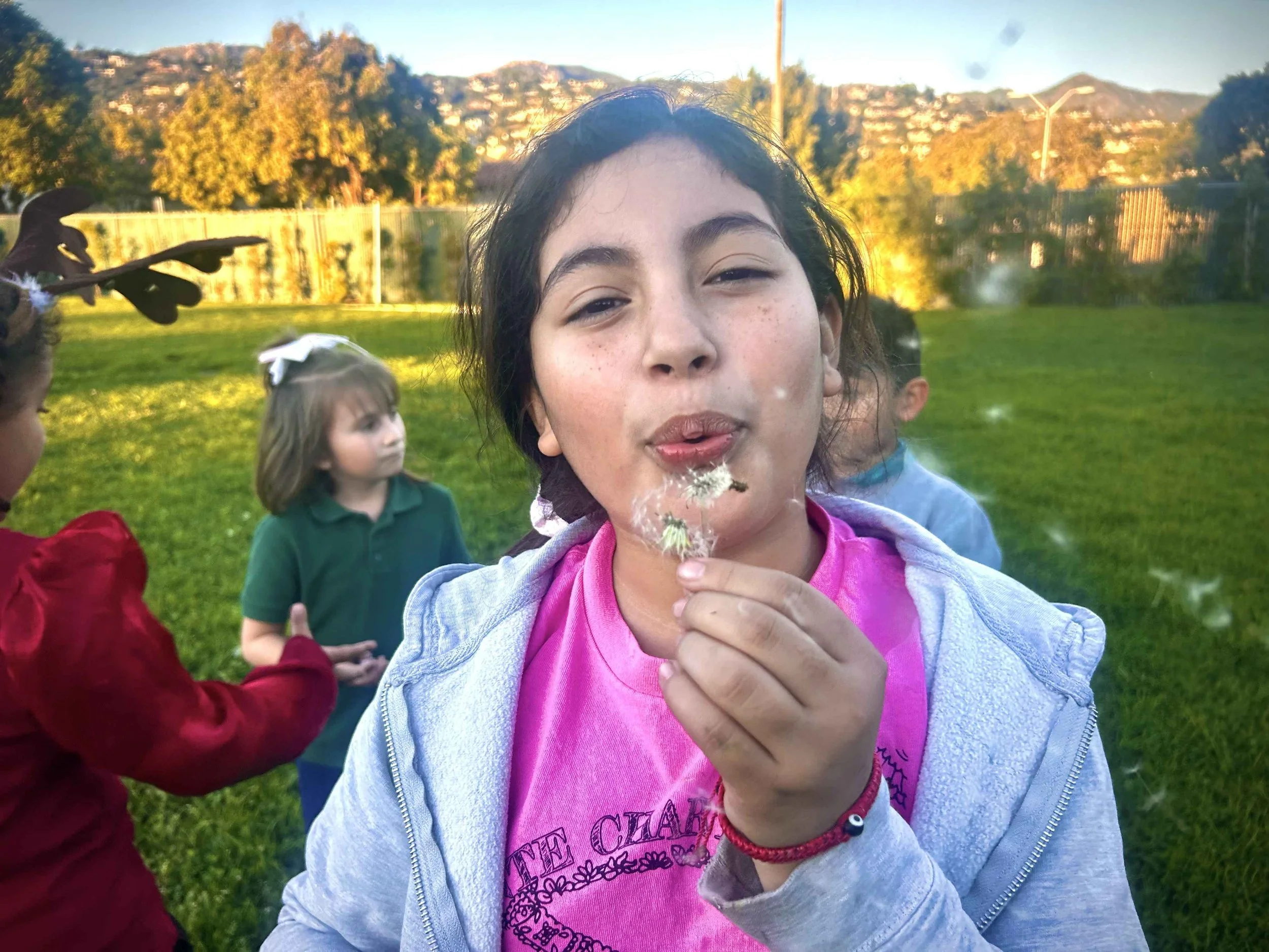 Girl blowing a dandelion at The Downtown Club after-school program in Santa Barbara.