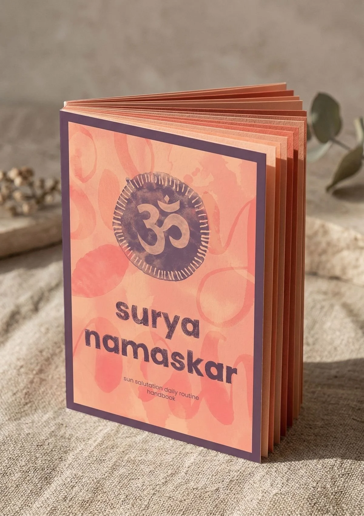 Book cover illustration for Surya Namaskar sun salutation handbook - warm peach and coral tones with a painted Om symbol and soft abstract shapes