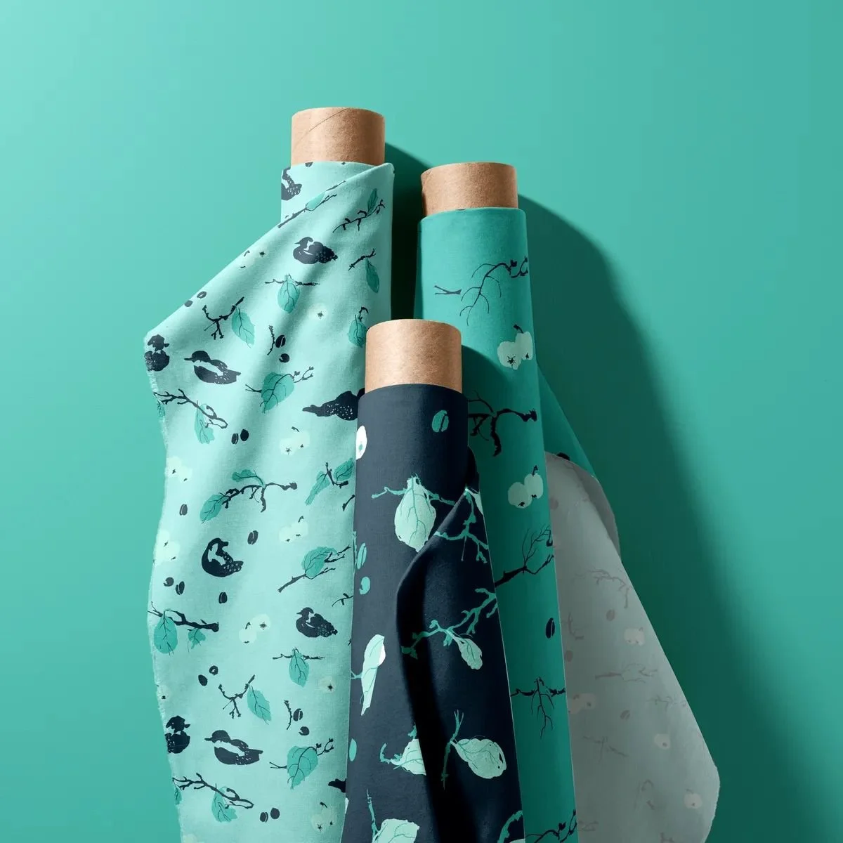 Three fabric rolls featuring the “Harvest in My Garden” pattern — plums, apples, birds, and leaves in cool greens.