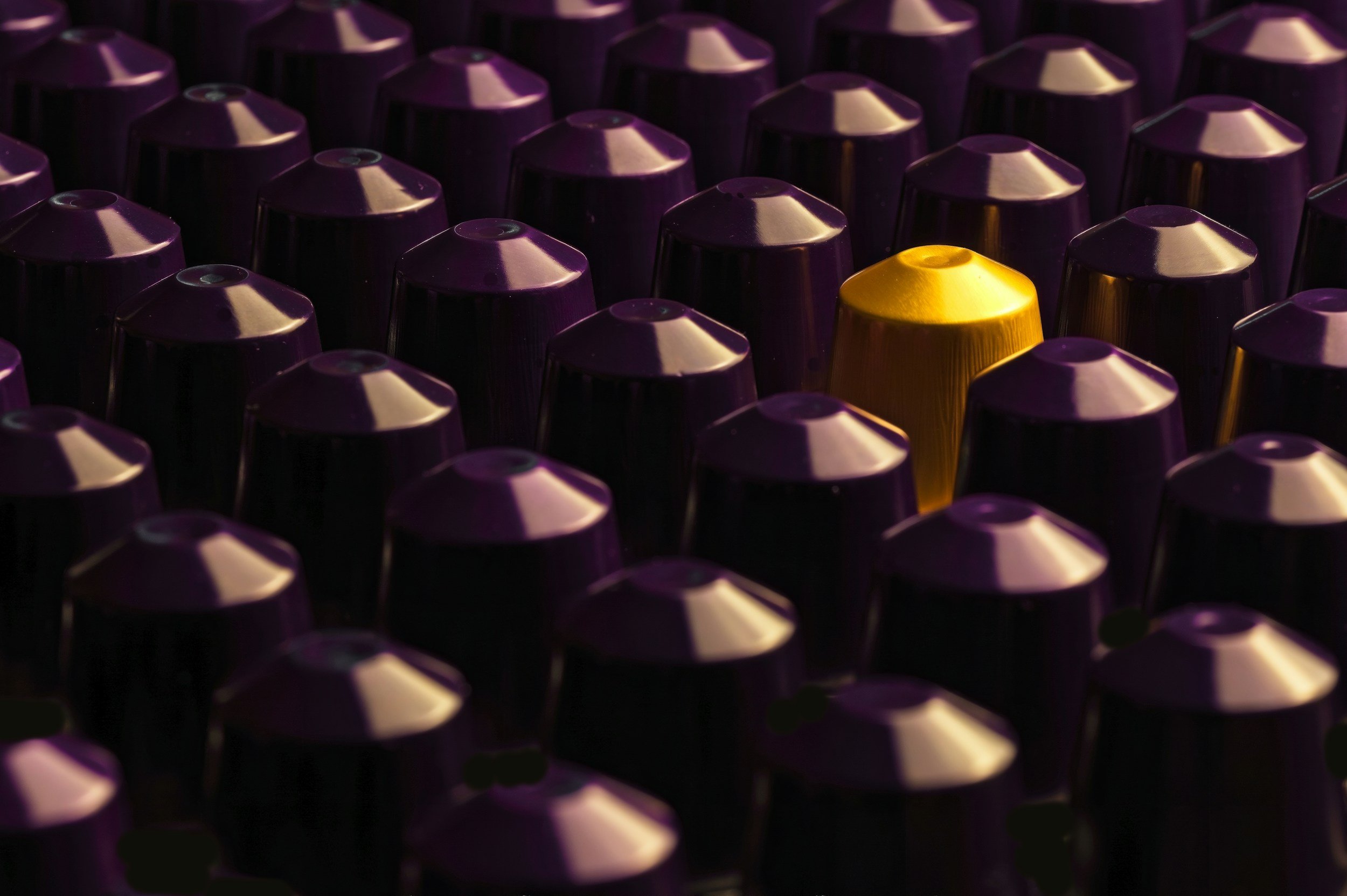 A close-up of multiple coffee capsules, mostly purple with one gold capsule among them.