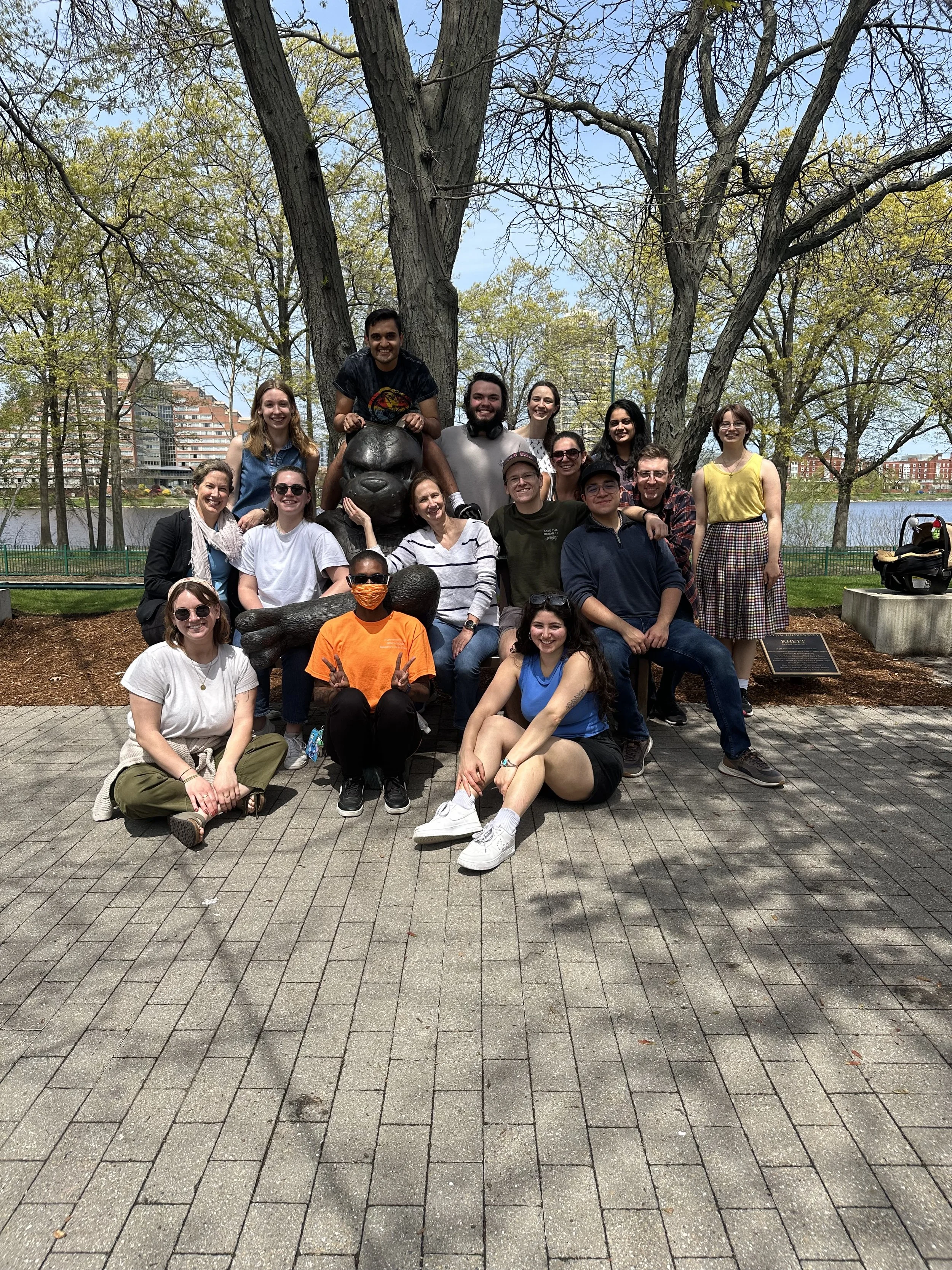 Group of people posing in front of a large gorilla sculpture outdoors on a sunny day with trees and buildings in the background.