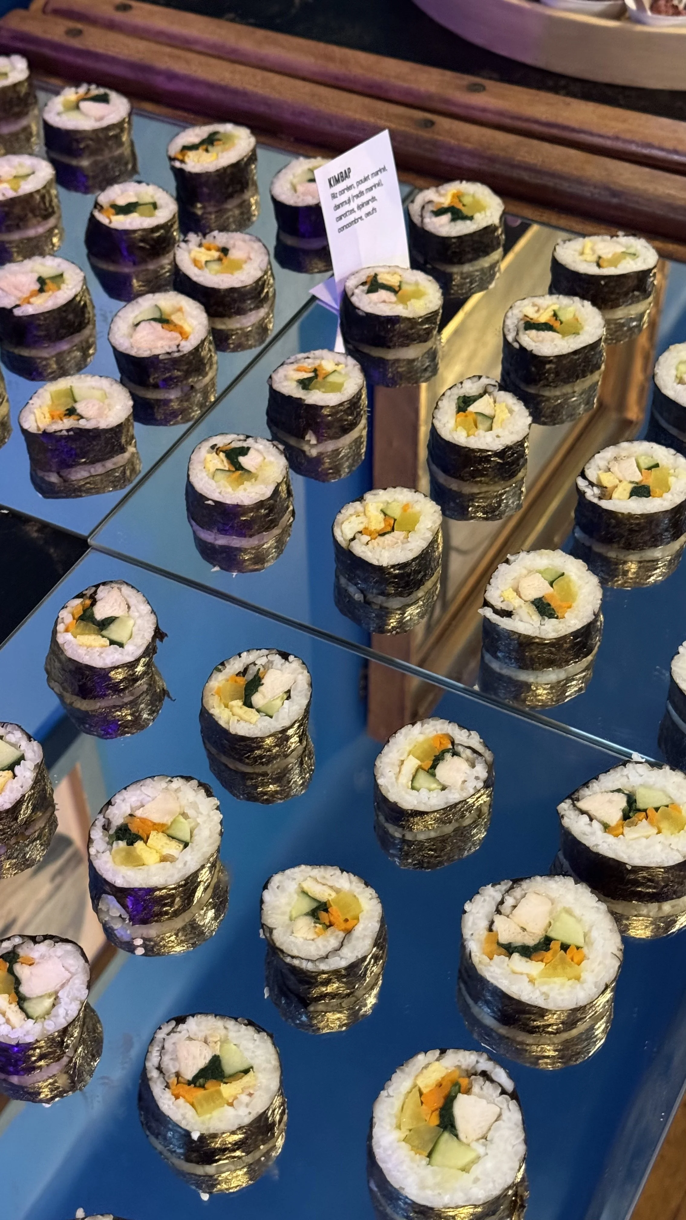 Des rouleaux de sushi avec du riz, des légumes, et du poisson, présentés sur une surface en miroir.