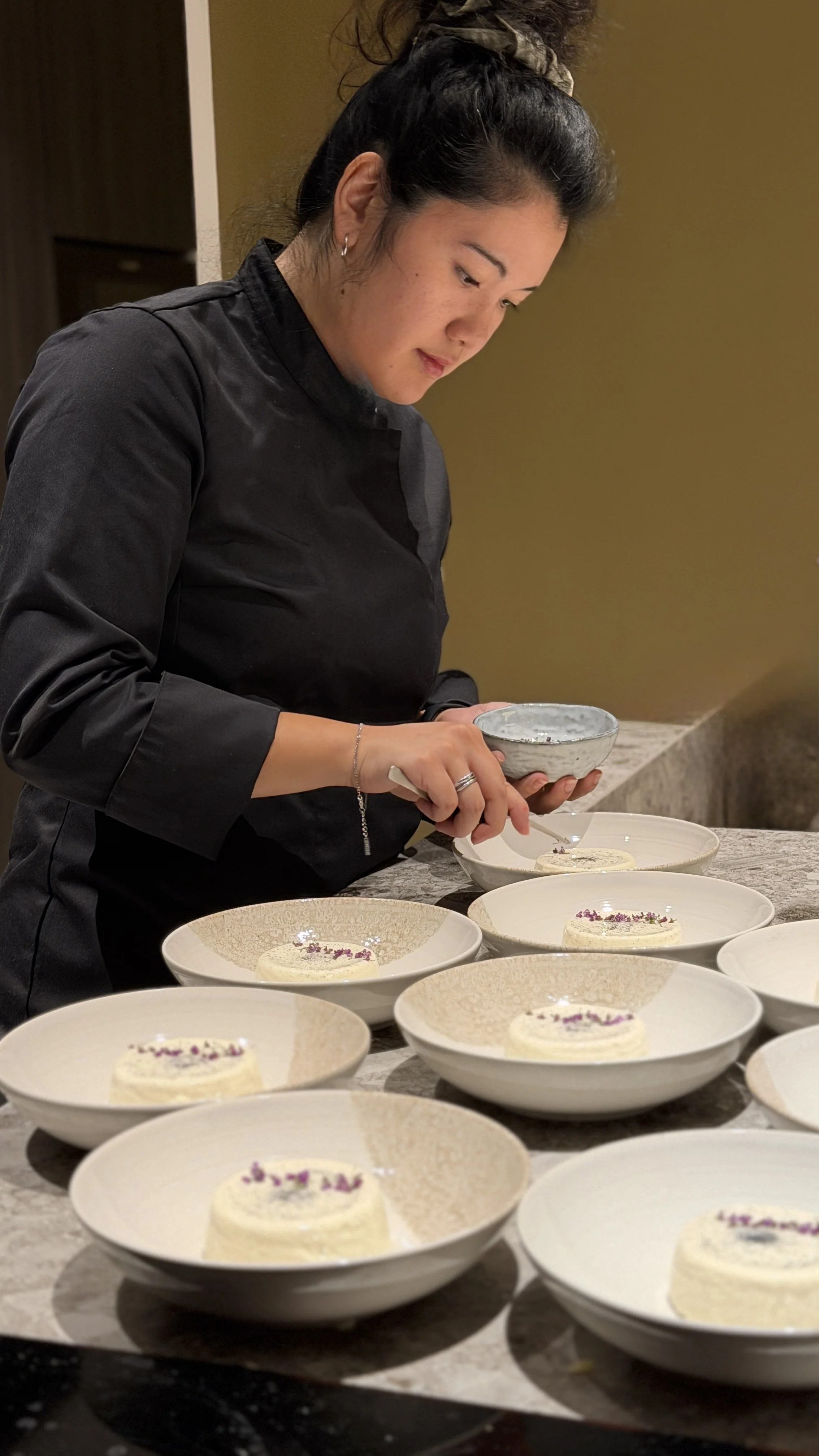 Une femme en uniforme de cuisine décore des desserts dans des assiettes sur un comptoir en marbre.