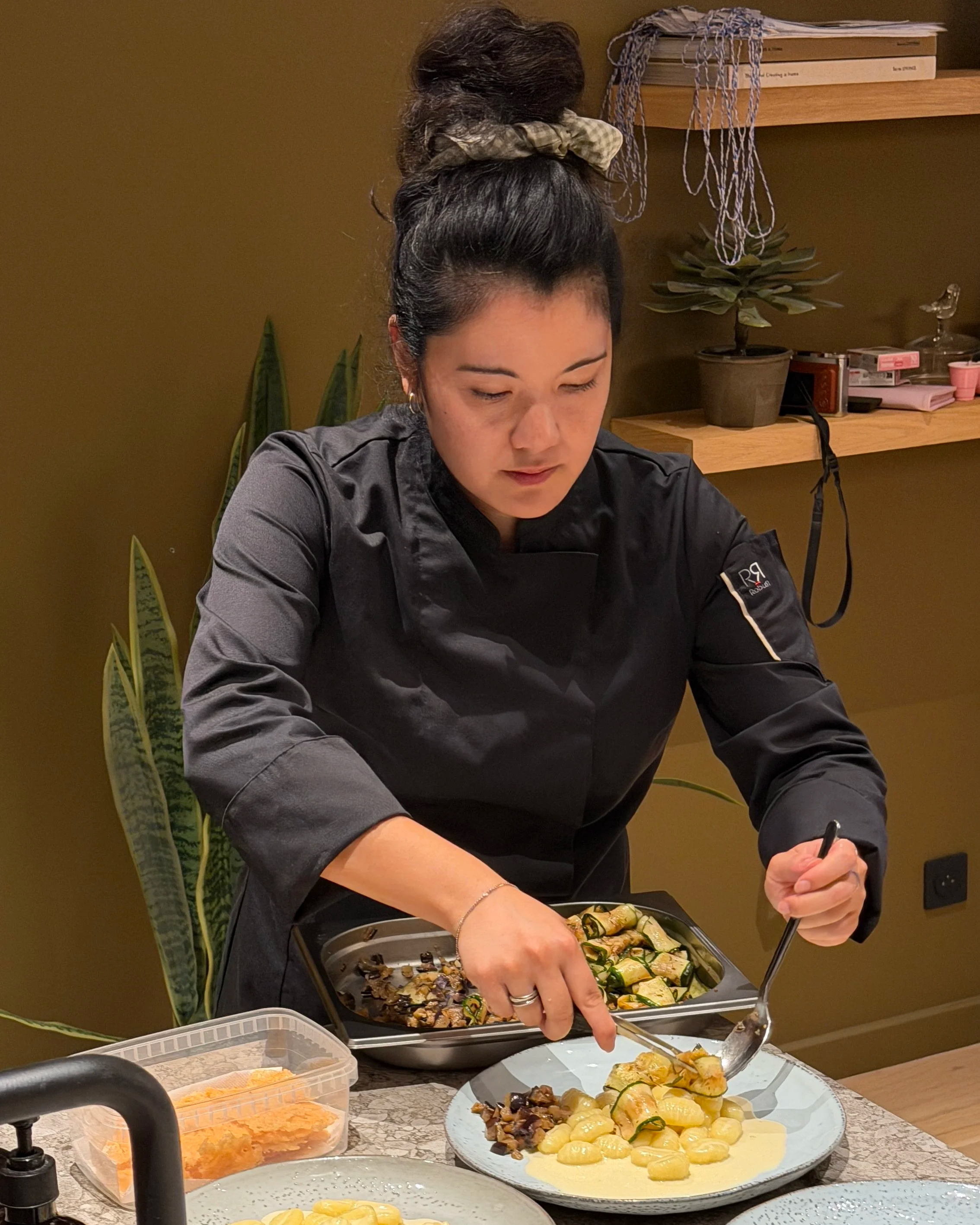 Une femme dresse un plat dans une assiette, avec des courgettes roulées, des légumes grillés dans une cuisine à Dijon pour un EVJF d'un groupe de femmes qui vient de l'étranger