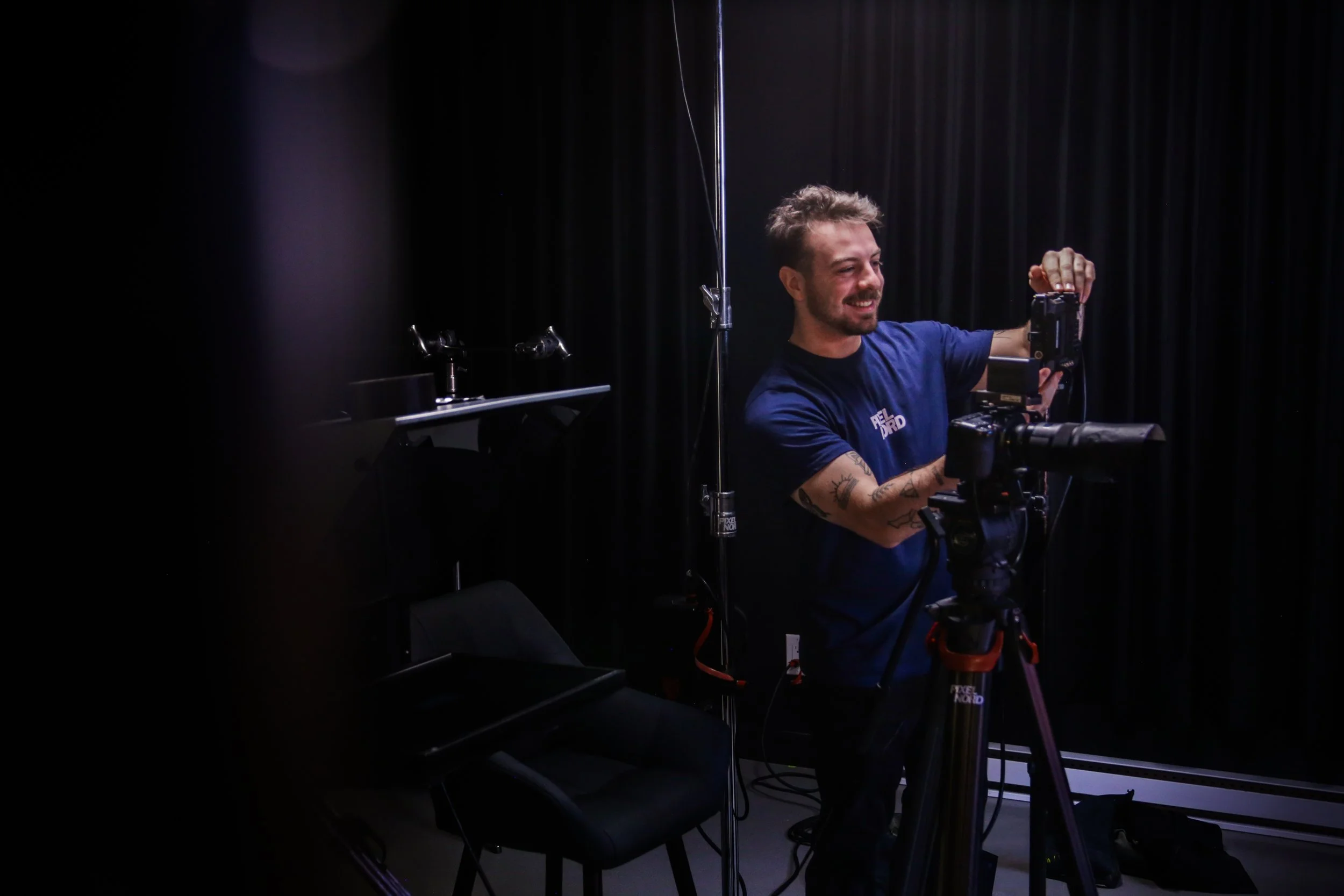 Un homme souriant en train de manipuler une caméra dans un studio avec un fond noir.