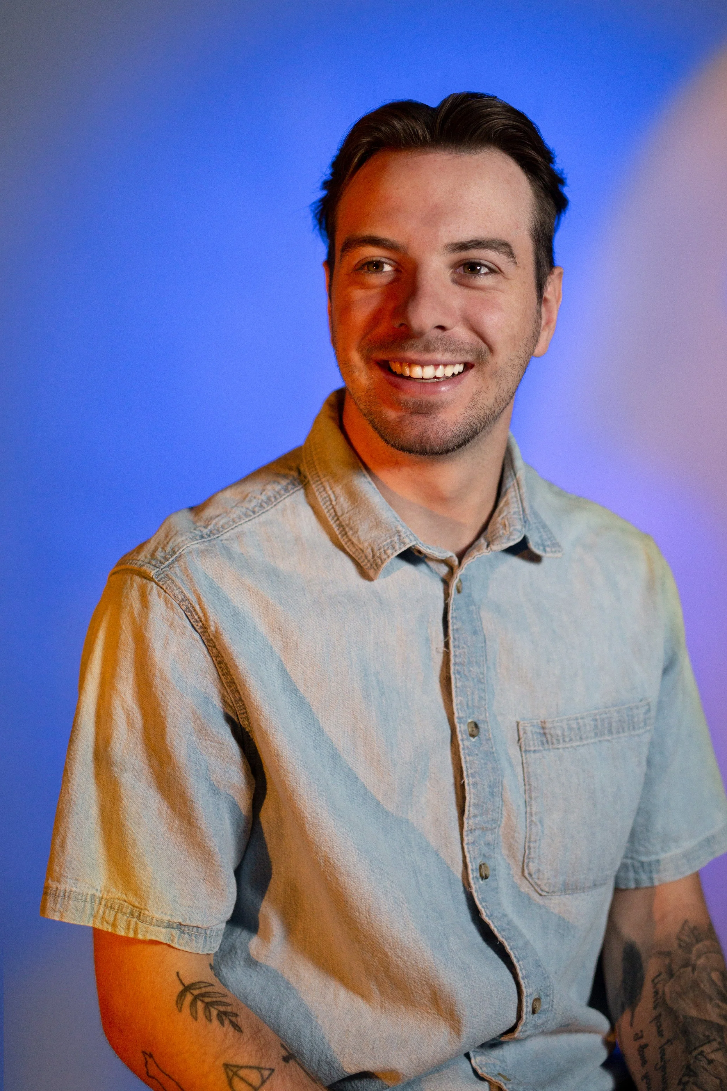 Un homme souriant avec une veste en jean clair, lumière colorée en arrière-plan