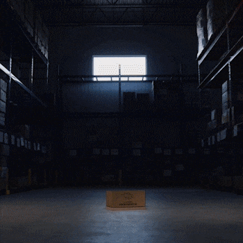 Un entrepôt avec des étagères remplies de caisses et une lumière naturelle venant d'une fenêtre en haut. Sur l'image, il y a une illustration d'un sac joyeux, représentant la fondation Rock-Guertin.