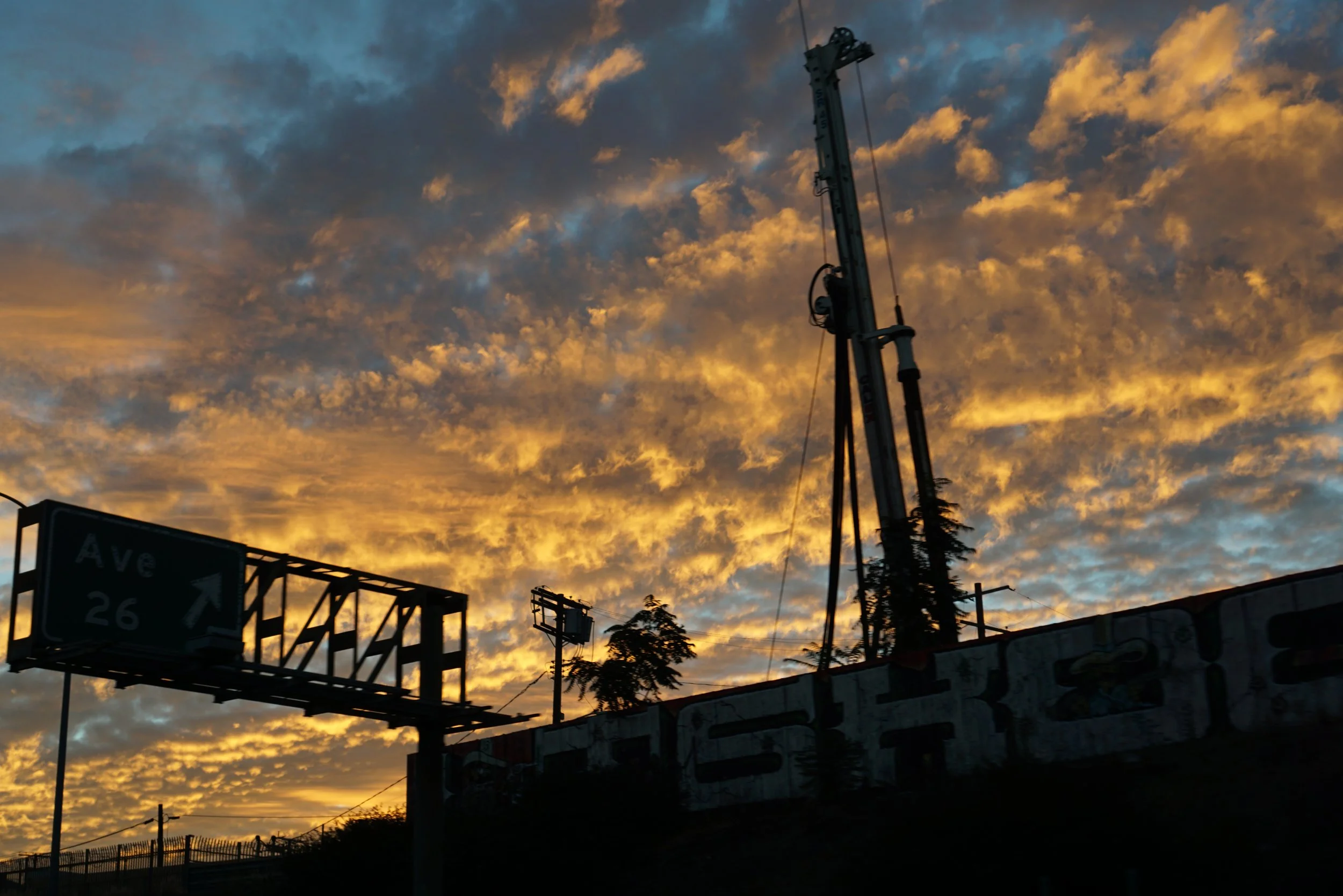 photo of a late sunset, the sky a bright blue and the clouds a bright orange. construction equipment, signs, and a building are silhouetted in front