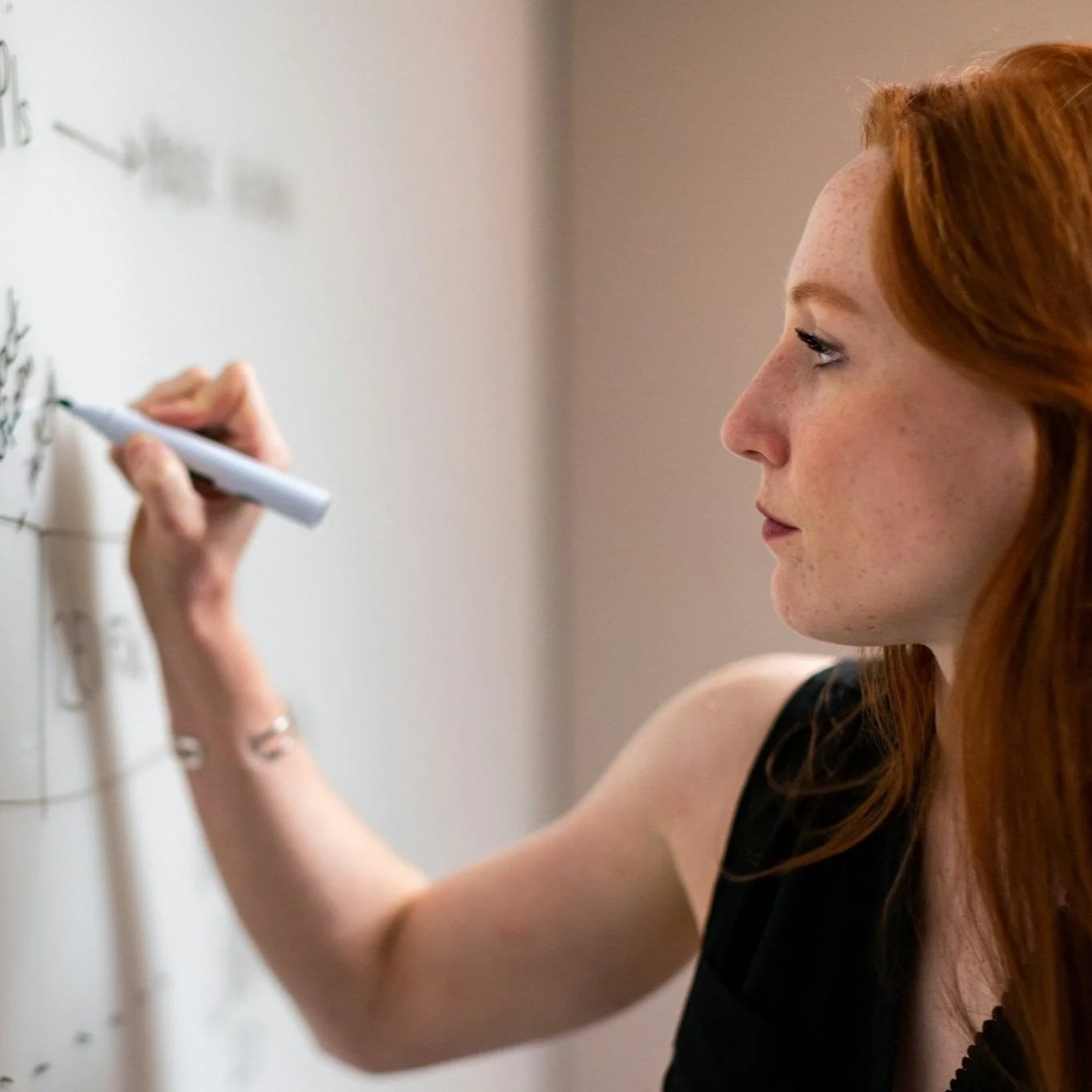 Red-haired woman writing on a whiteboard with a marker