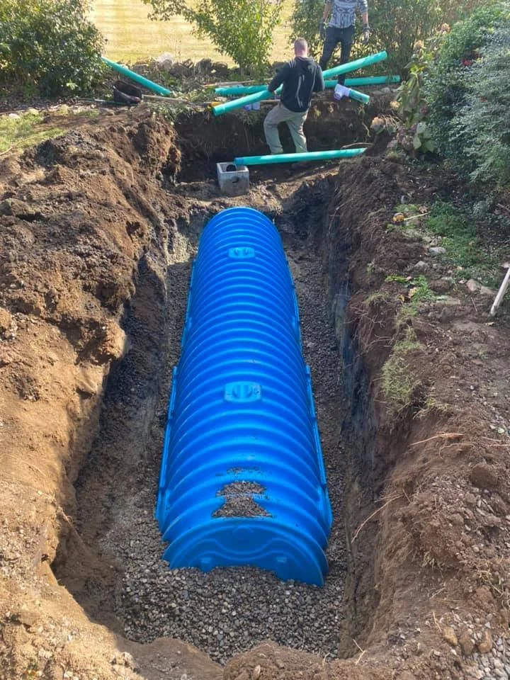 Workers installing an underground sewage field in a dirt trench, surrounded by 3/4 washed stone, topped off with filter fabric and topsoil.