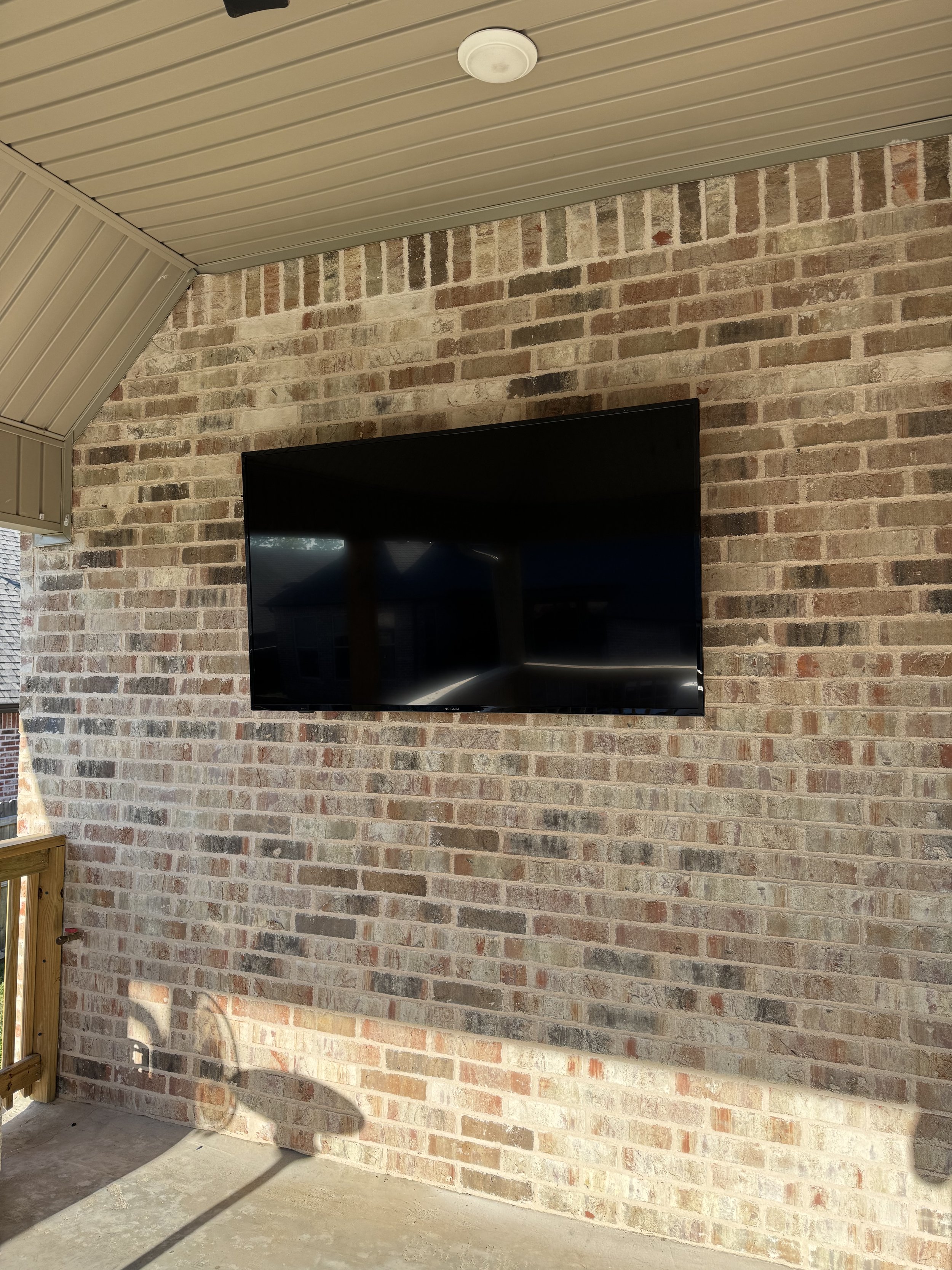 Flat-screen TV mounted on a brick wall of a covered outdoor patio area.