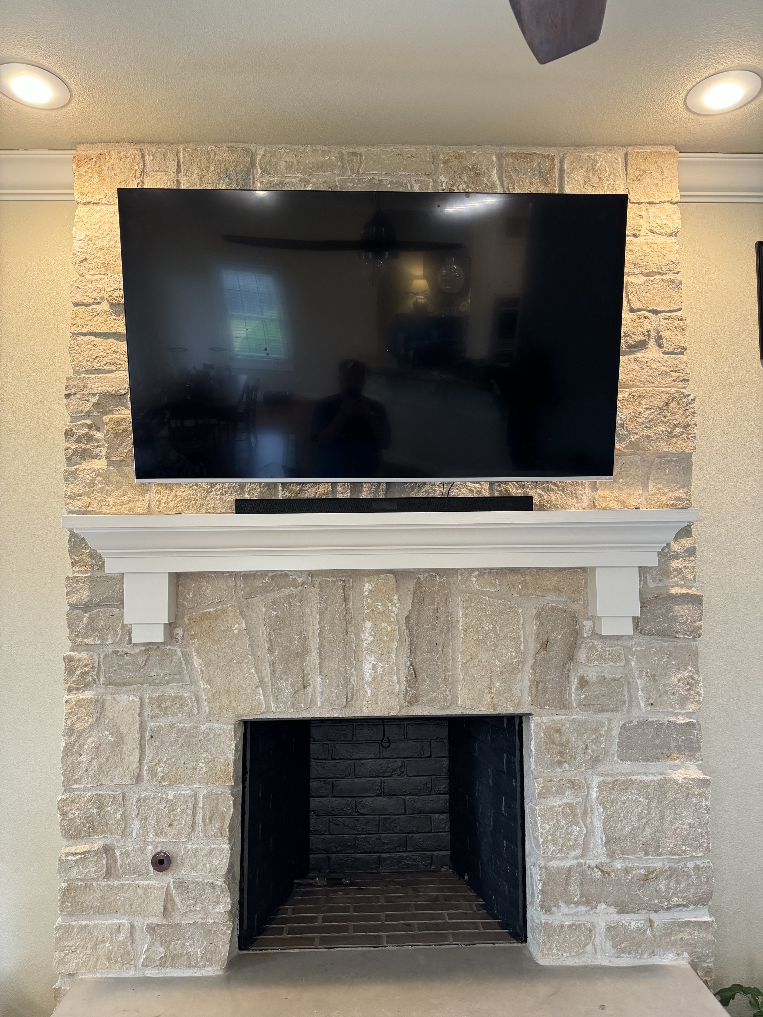 Stone fireplace with a mounted flat-screen TV above: a white mantel shelf and a black interior of the fireplace.