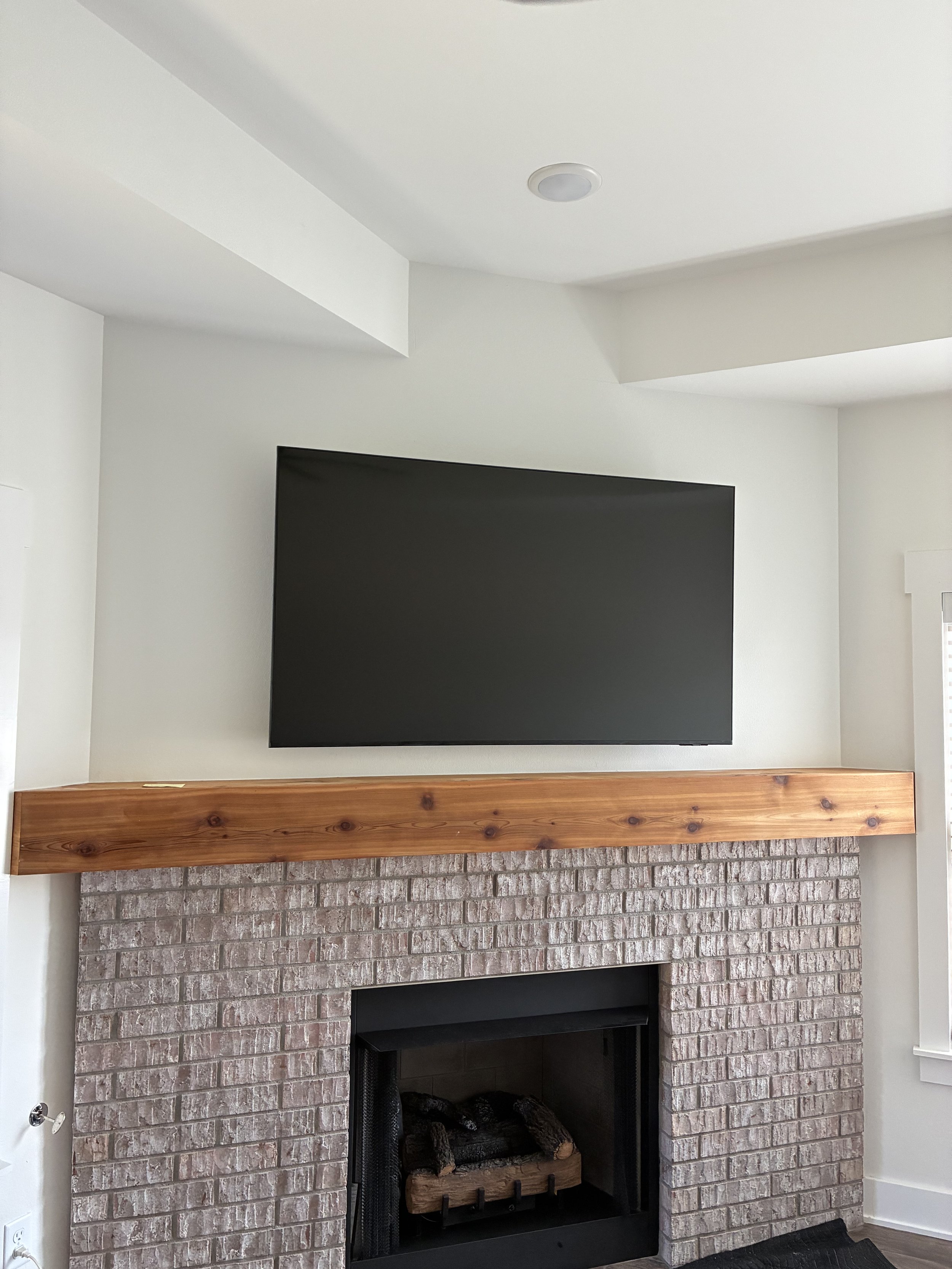 Living room fireplace with a brick surround, wooden mantel, and a mounted flat-screen TV above.