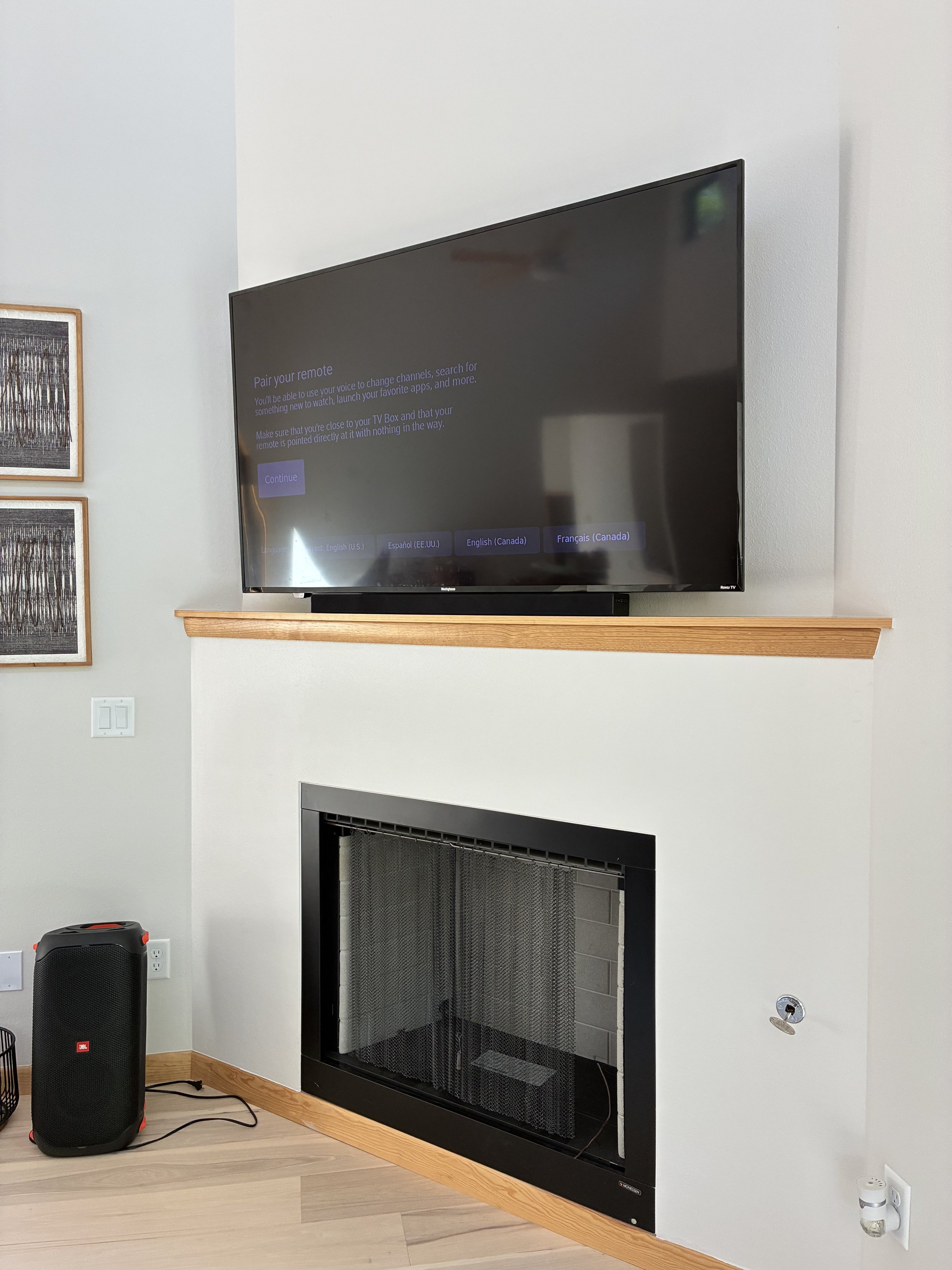 Living room fireplace with a mounted flat-screen TV above it, and a JBL speaker on the floor to the left.