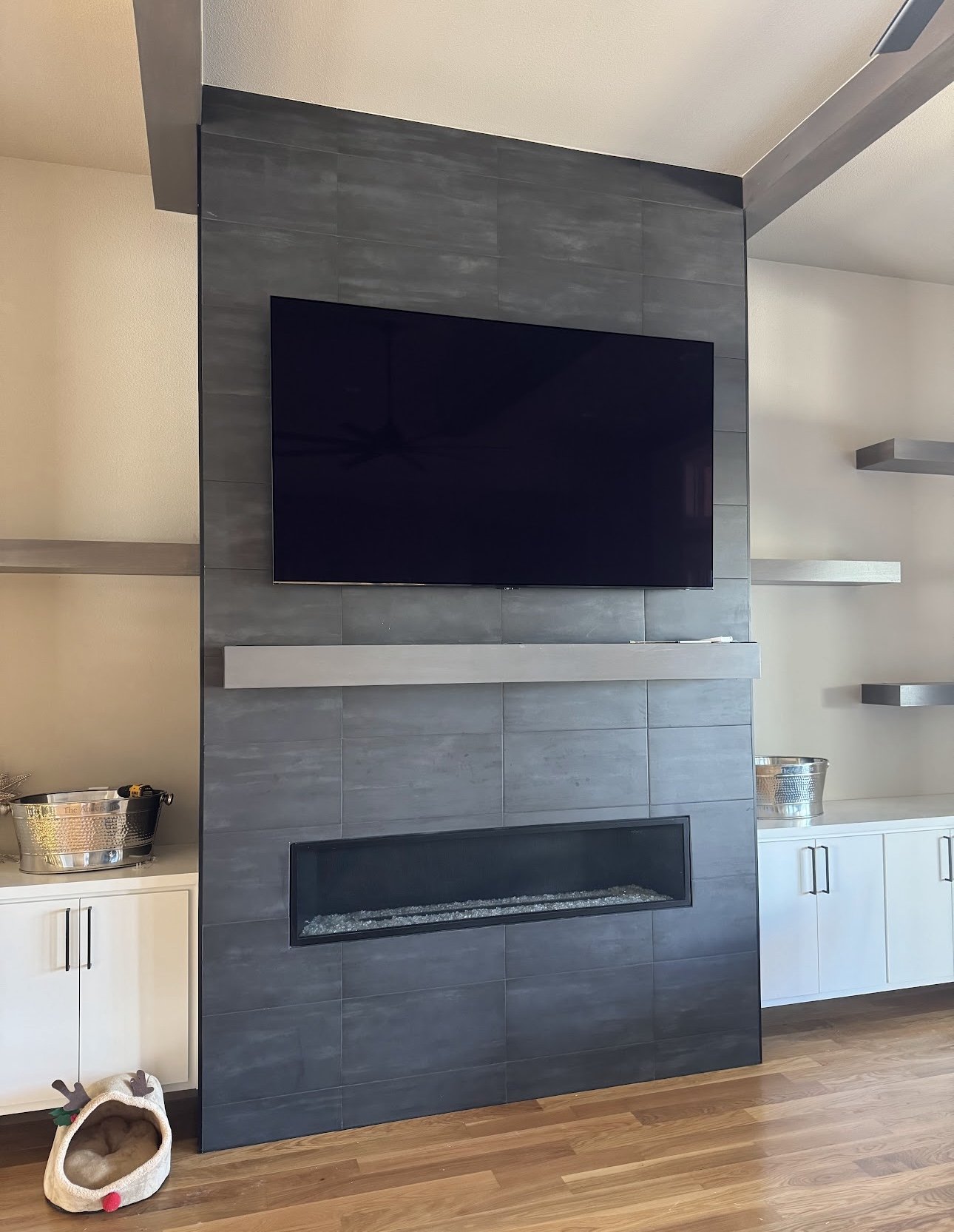 Modern fireplace with a mounted flat-screen TV above it, surrounded by gray tiles, with two white cabinets and shelves nearby.
