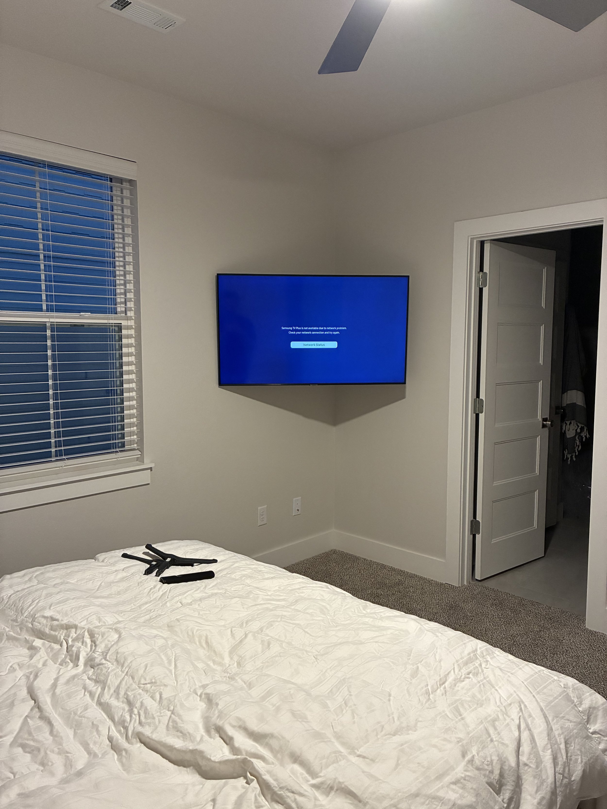 A bedroom with a bed, a window with blinds, a wall-mounted TV displaying a network error, and an open door revealing a closet.