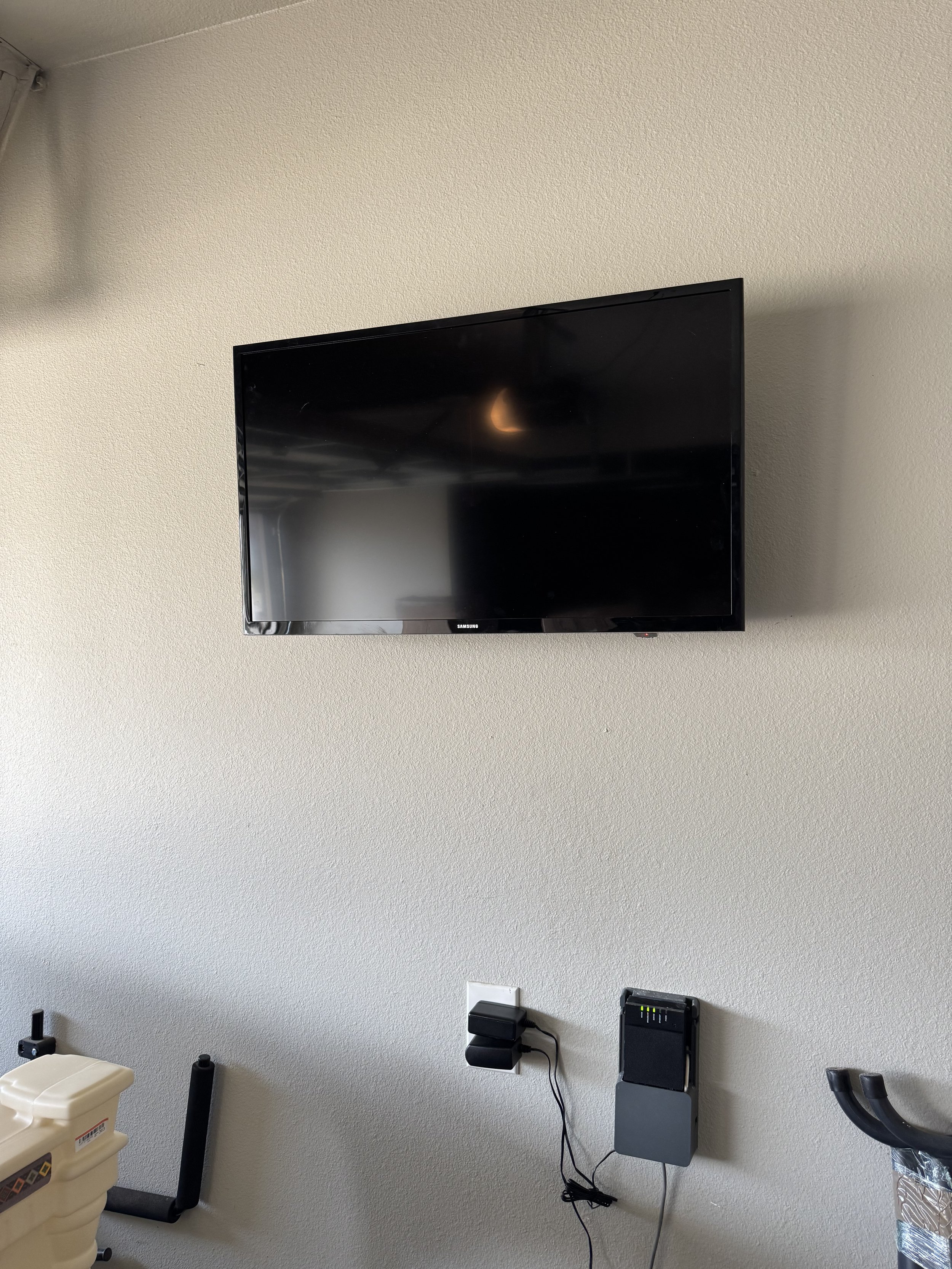 A flat-screen television mounted on a beige wall in a room with various electronic devices and objects below it.