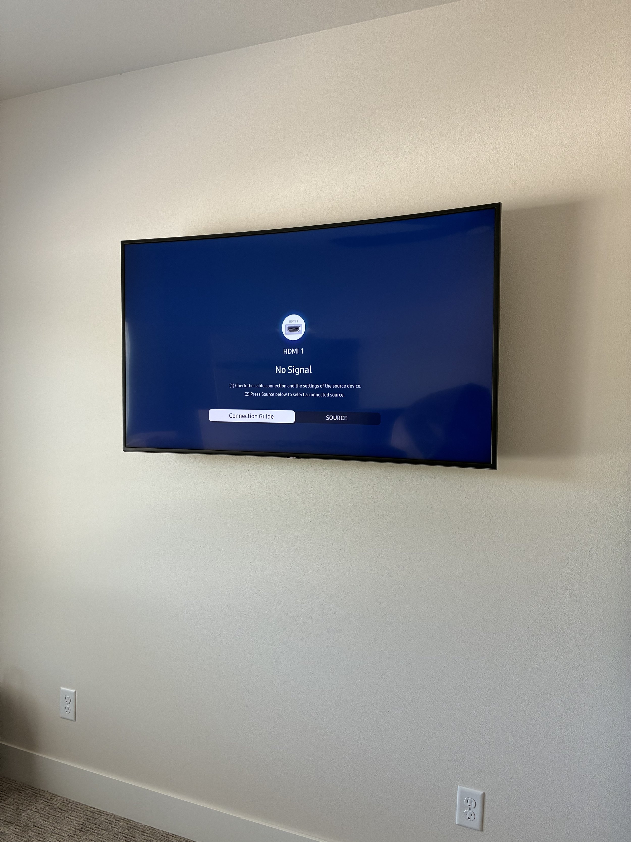 A flat-screen television mounted on a white wall displays a 'No Signal' message with options for connection guidance and source selection.