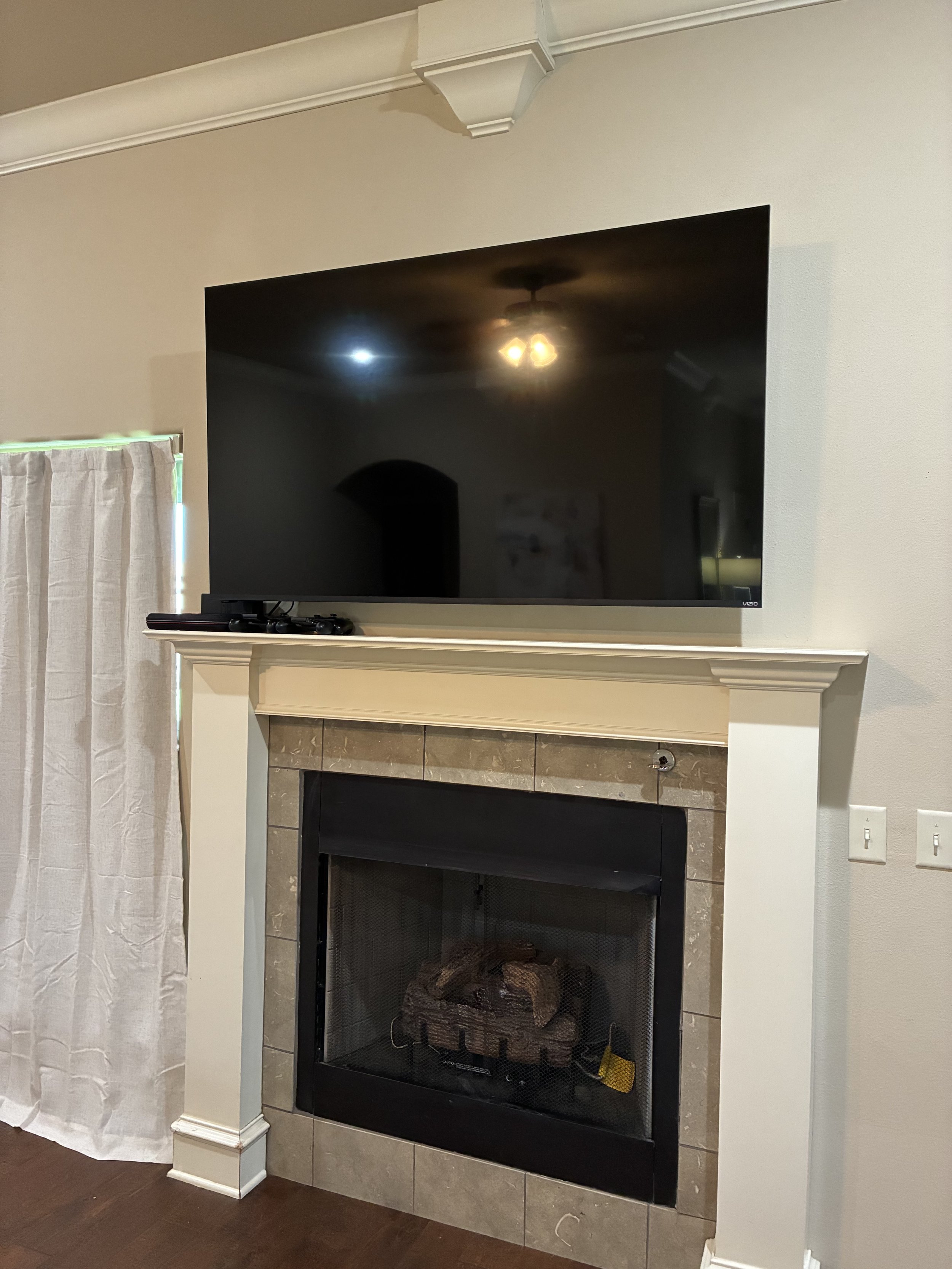 Flat-screen TV mounted above a fireplace with wood logs inside, and beige tiles around the fireplace opening.