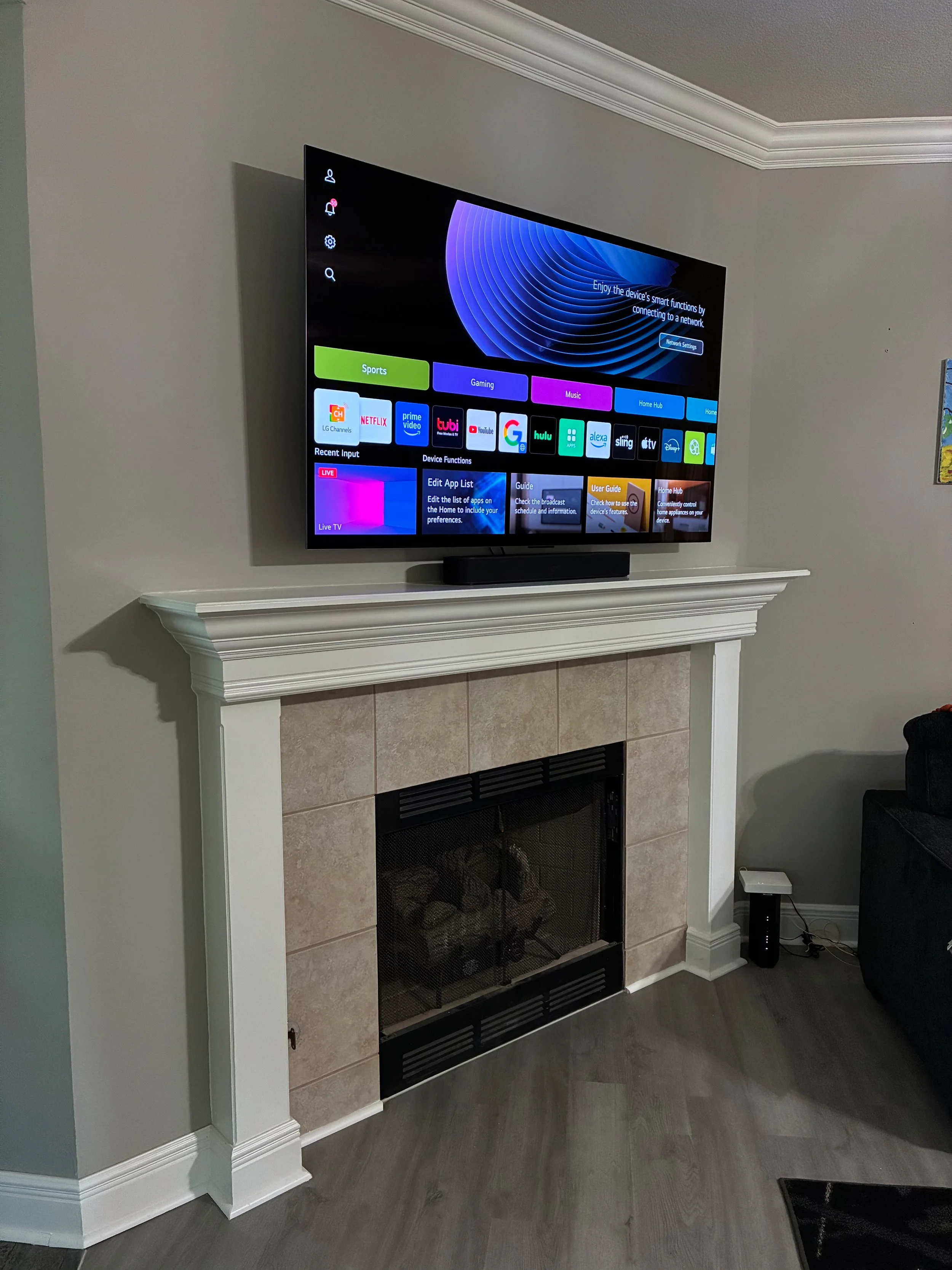 Living room fireplace with a mounted flat-screen TV displaying a smart TV interface above the white mantel, and a black soundbar on top of the mantel.