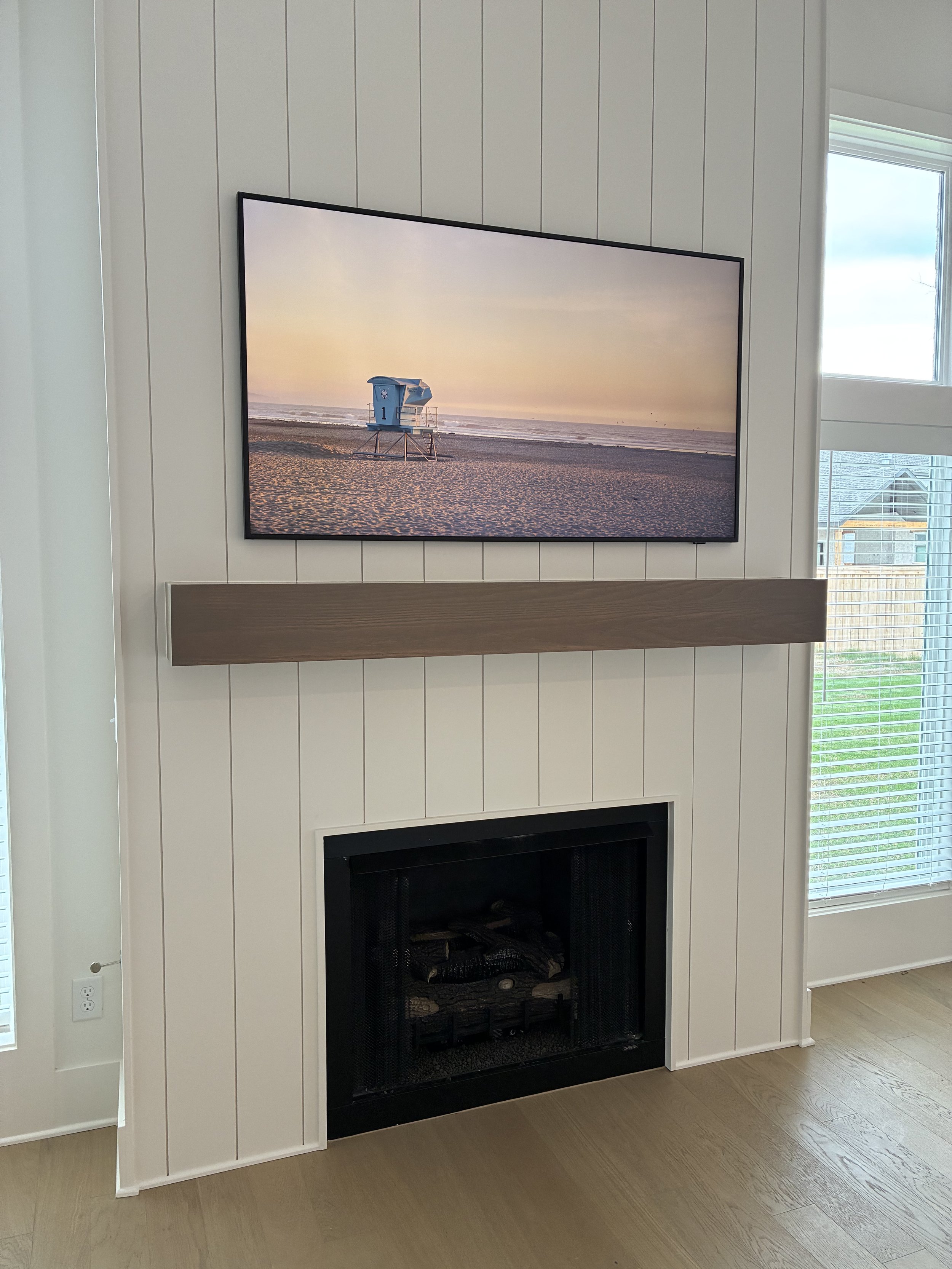 Living room fireplace with a wall-mounted flat-screen TV displaying a beach scene with a lifeguard tower at sunset.