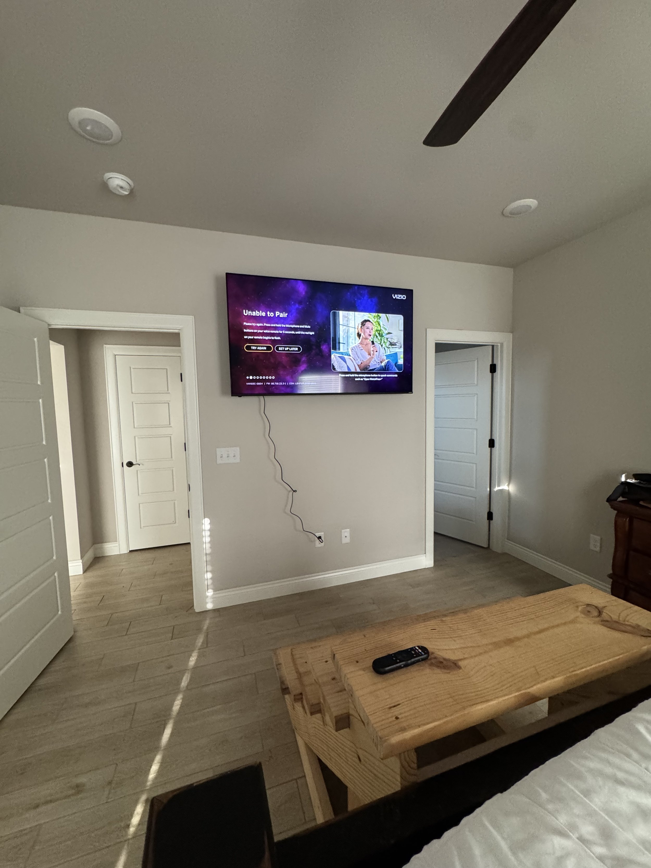 Living room with a wall-mounted TV displaying an error message, a door, a ceiling fan, and a wooden bench with a remote control on it.