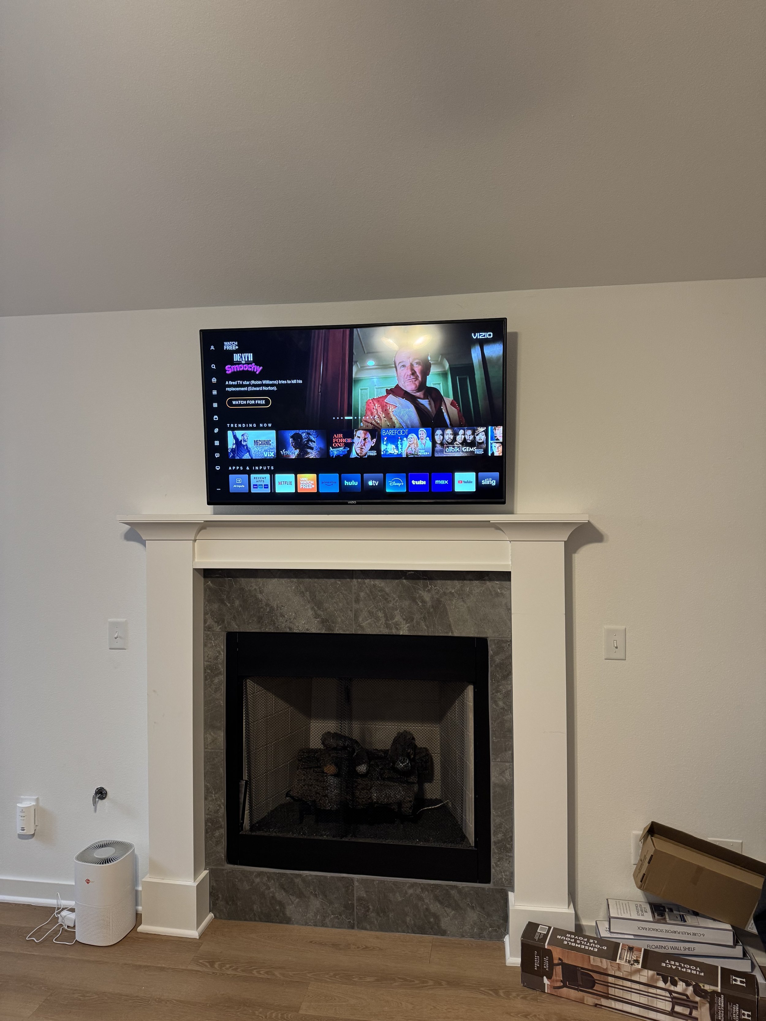 Living room fireplace with TV mounted above, displaying a streaming service interface, with some boxes on the floor to the side.