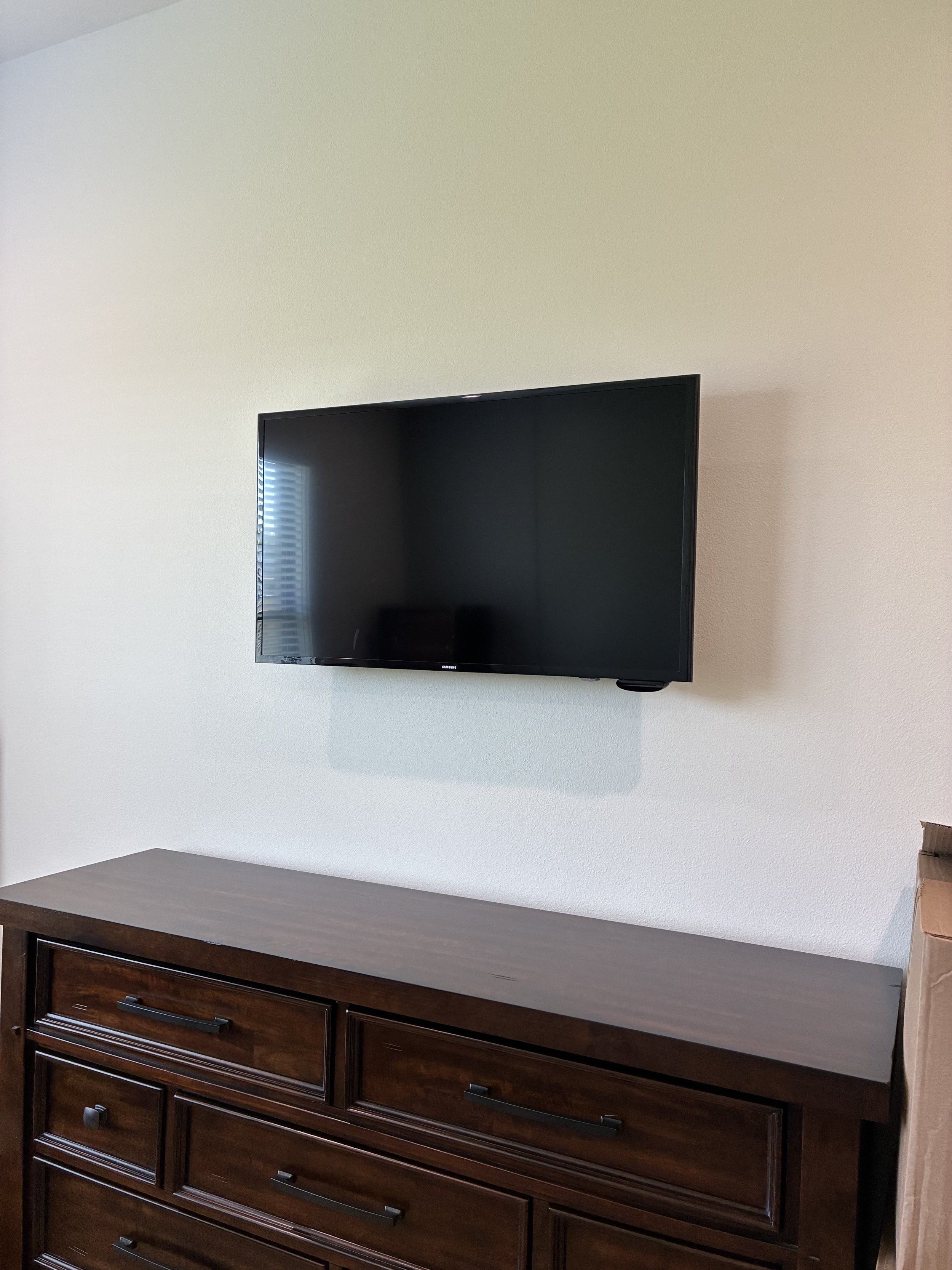 Flat-screen TV mounted on a white wall above a dark wooden dresser.