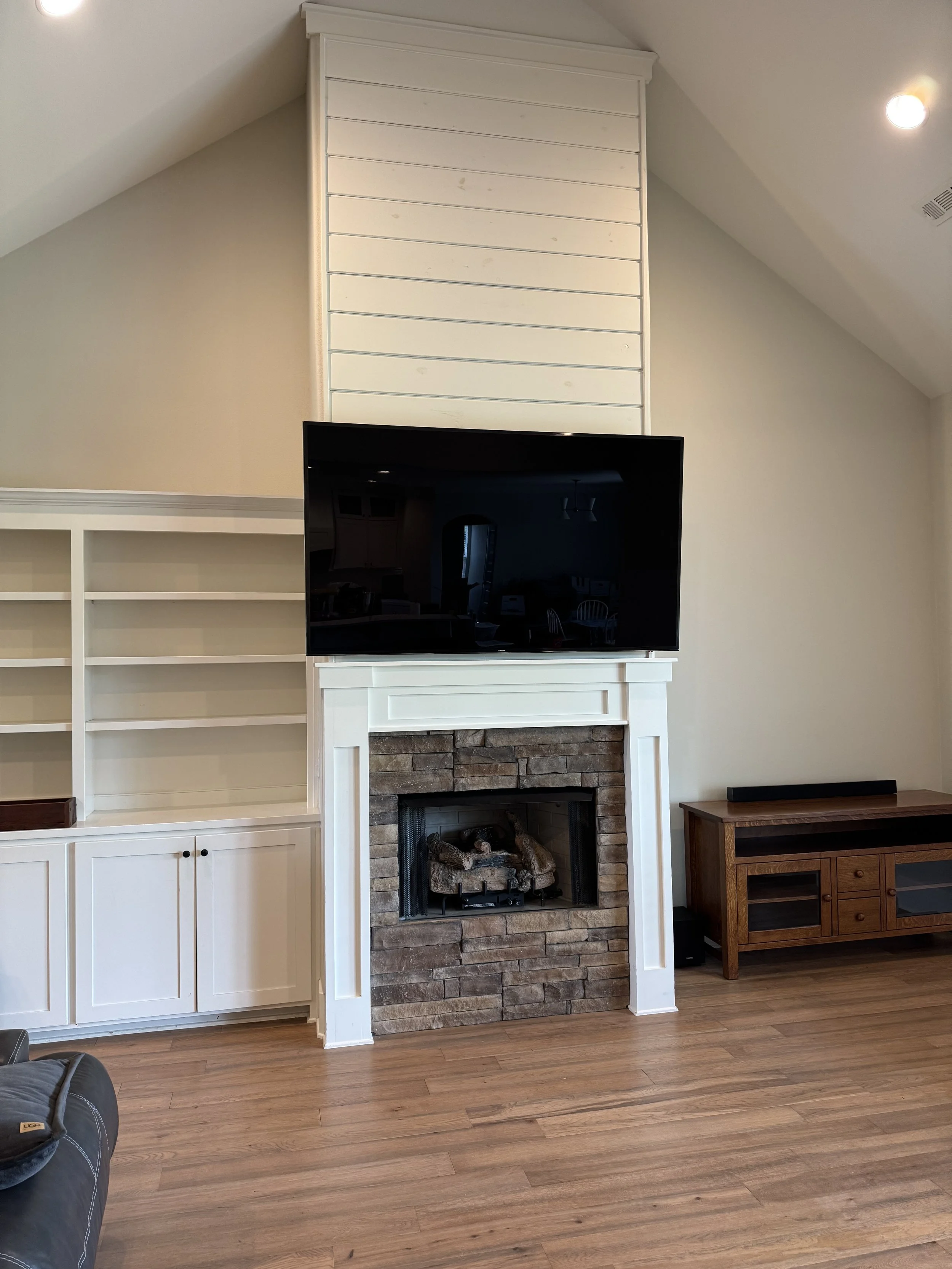 Living room with a built-in white cabinet and shelves, a stone fireplace with a flat-screen TV mounted above, and a wooden console table on the right side.