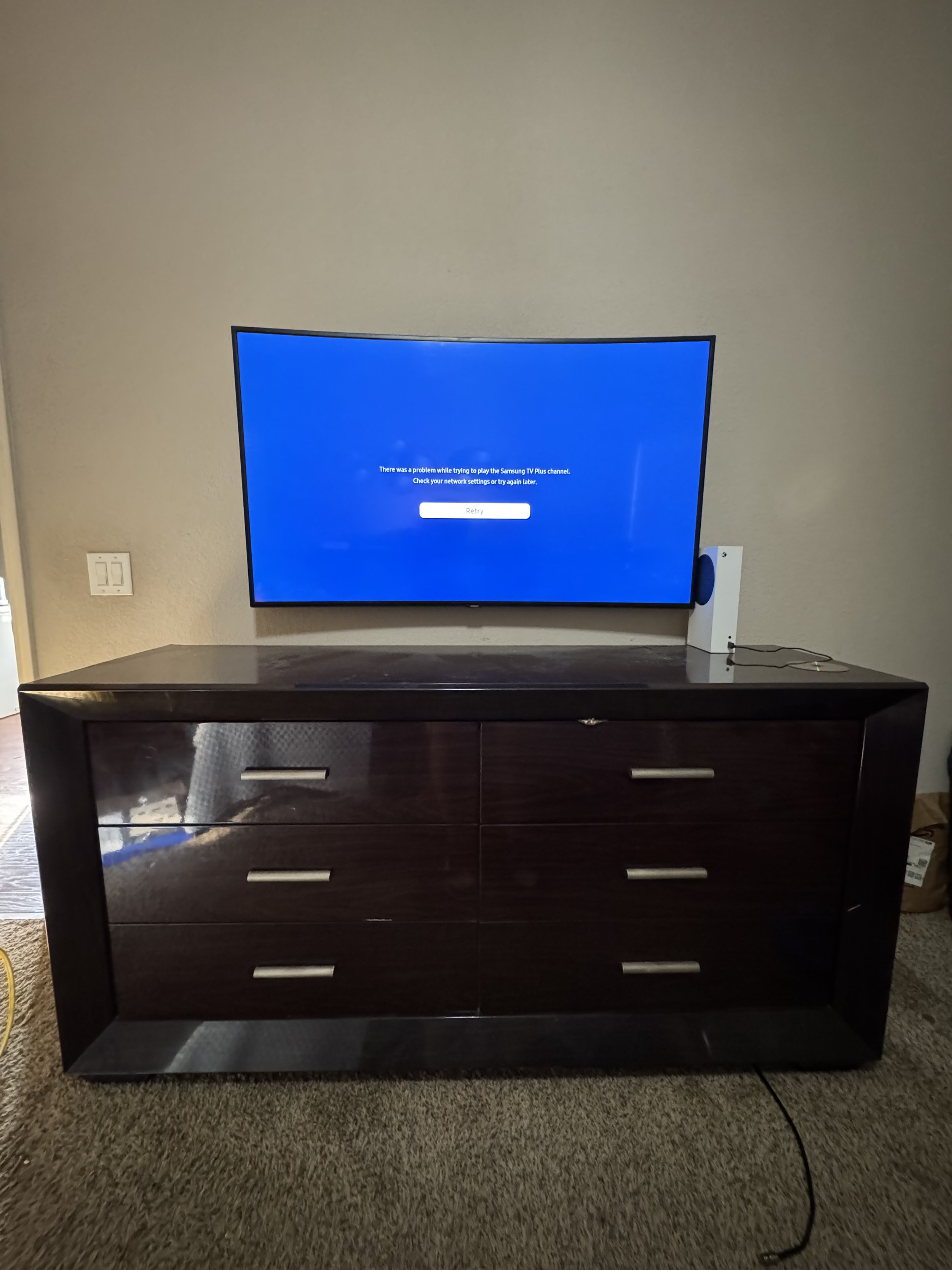 Flat-screen television on top of a dark wooden dresser, displaying a blue error message, with a speaker on the right side and a wall with a light switch in the background.