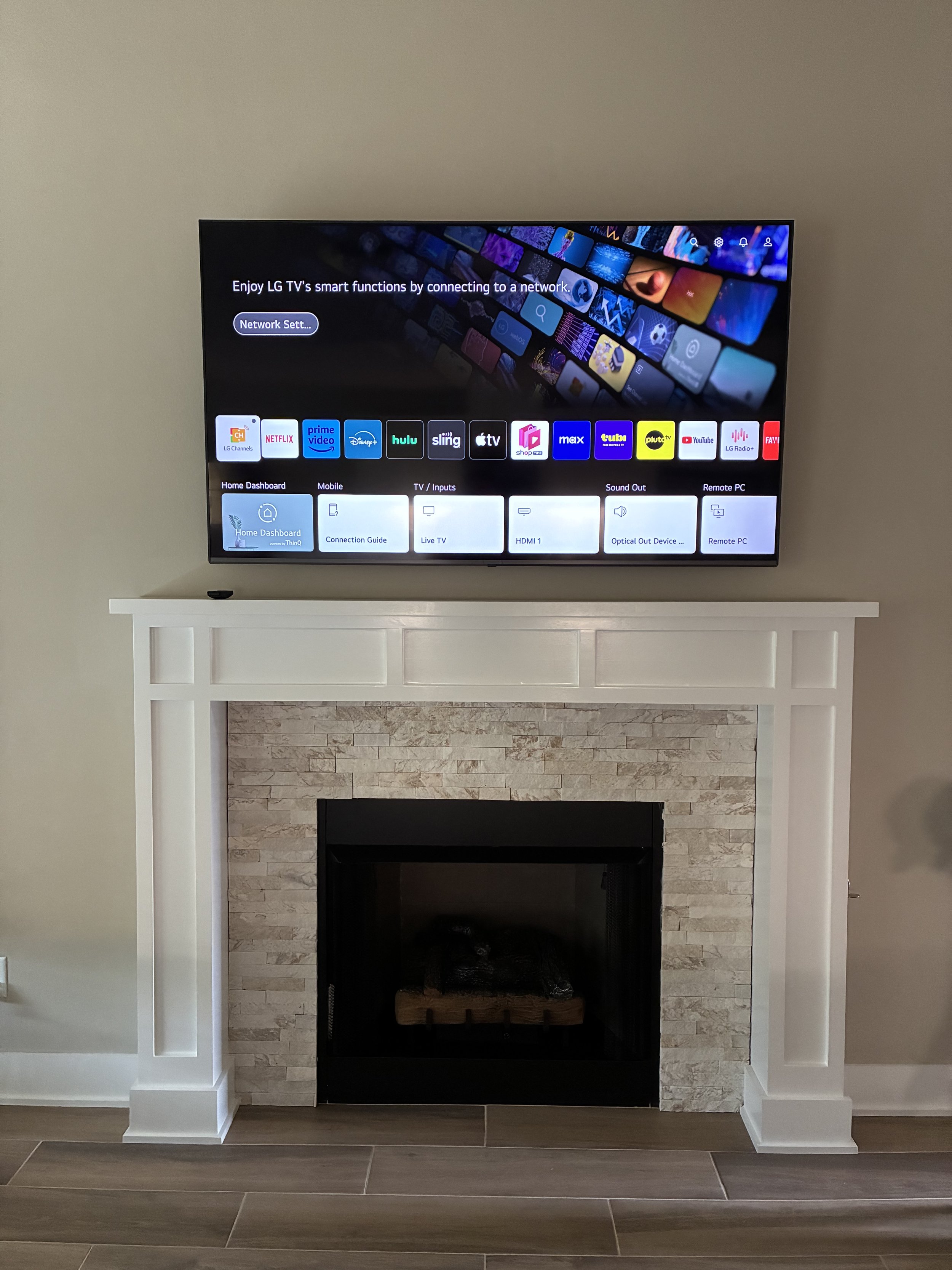A flat-screen TV is mounted above a white fireplace mantel with a brick surround, showing a smart TV interface.