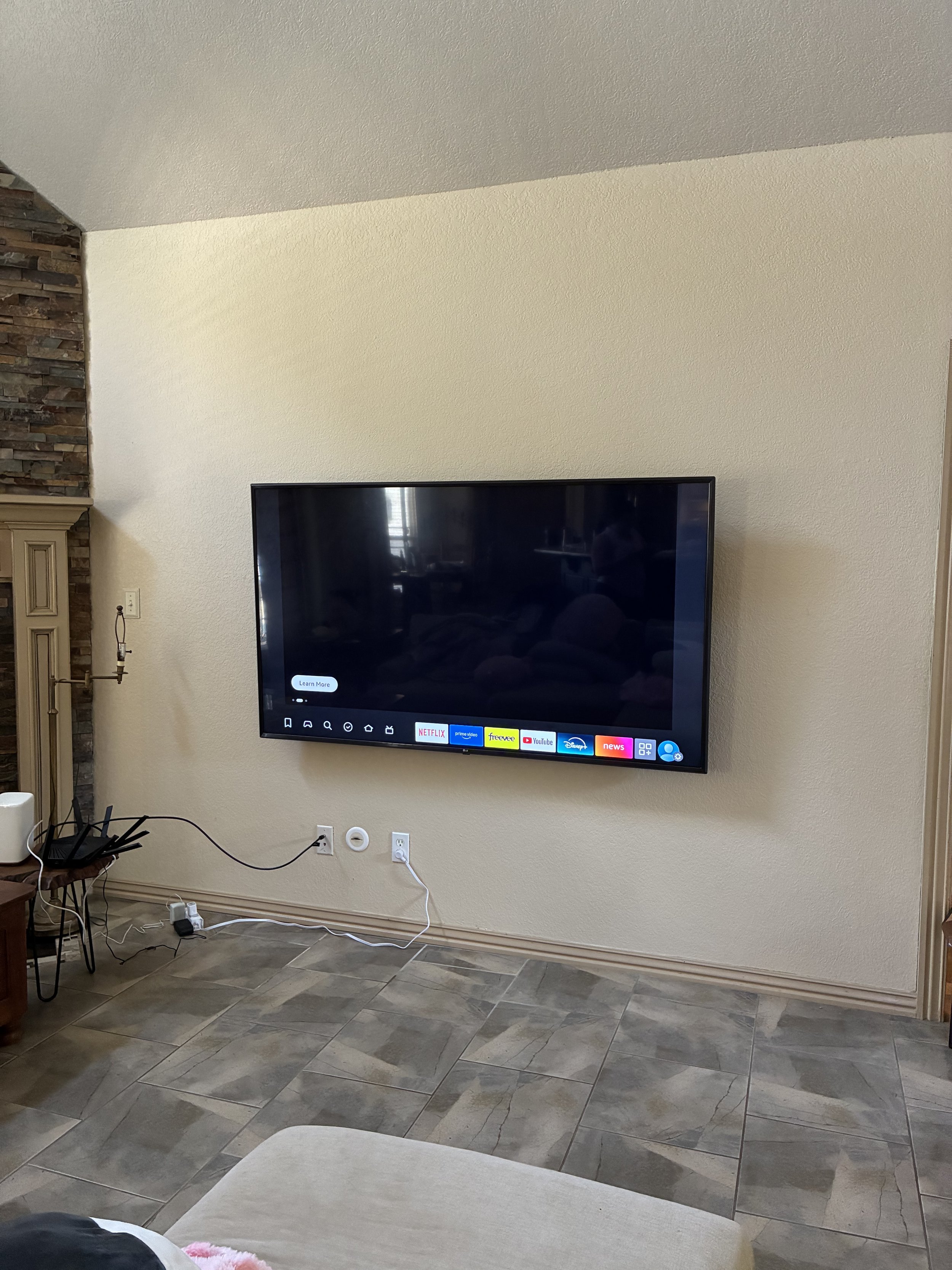 Living room with a mounted flat-screen TV displaying streaming service icons on the screen, beige walls, and tiled flooring.