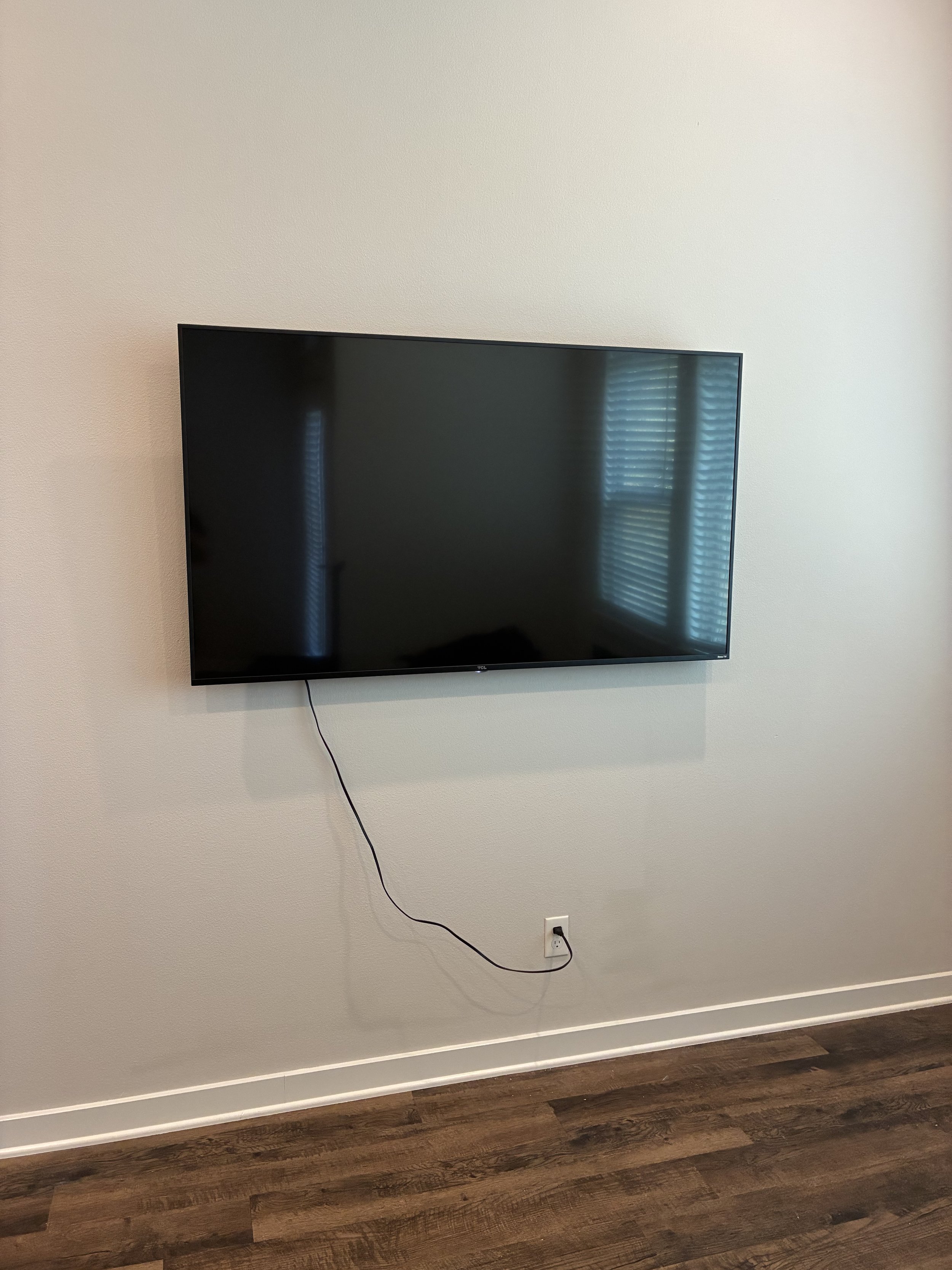 A flat-screen TV mounted on a white wall with a power cord hanging down to an electrical outlet.