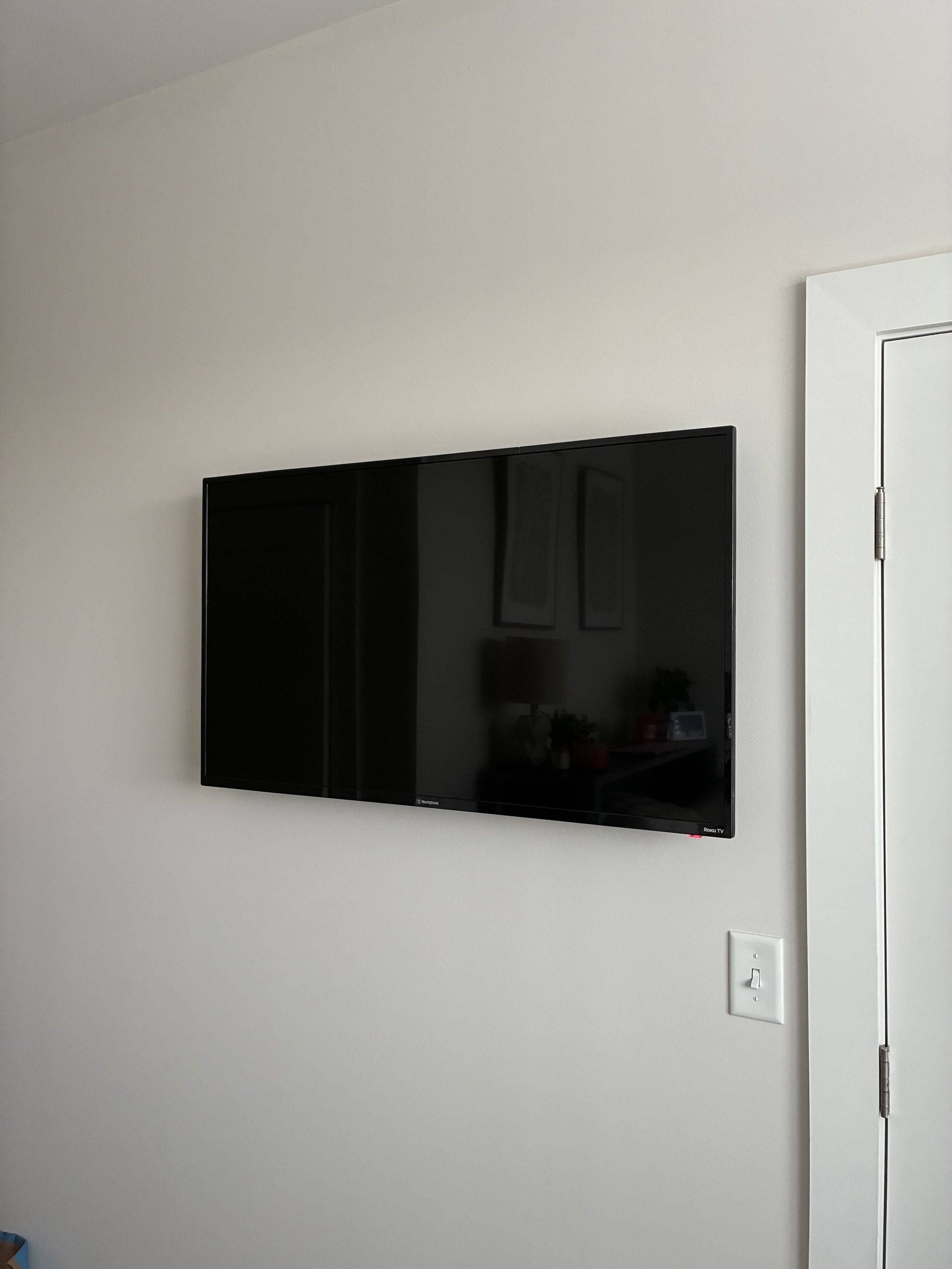 A flat-screen TV mounted on a white wall near a white door with a light switch beside it.
