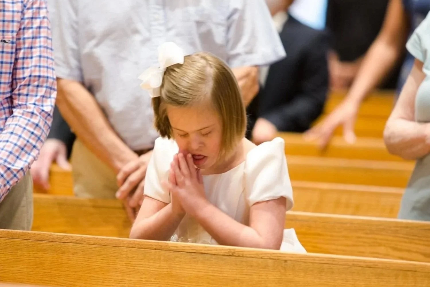Young girl praying with hands pressed together inside a church, surrounded by adults.