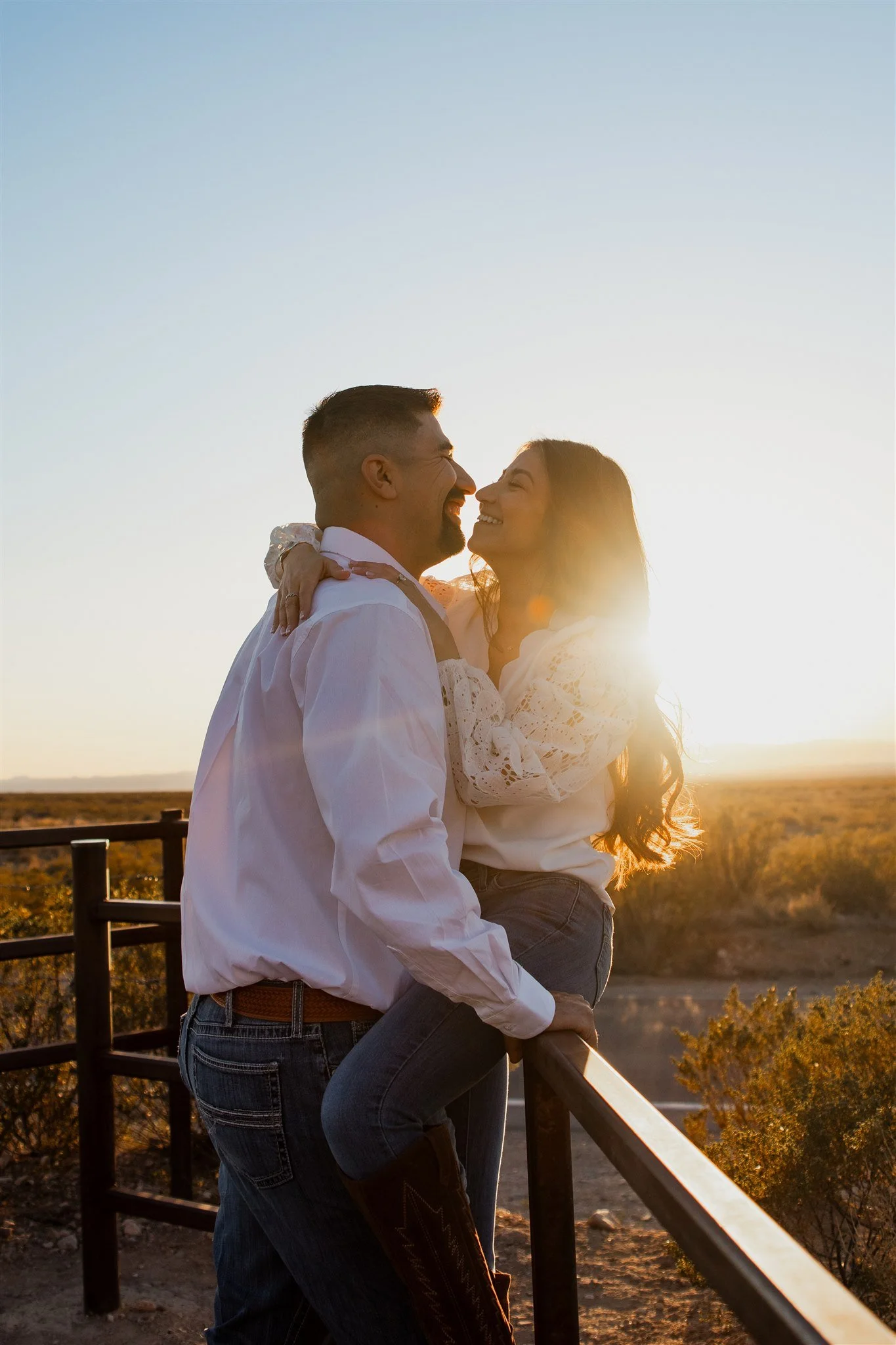 A couple smiling and looking at each other during sunset in a desert landscape, with the woman being carried by the man and embracing him.