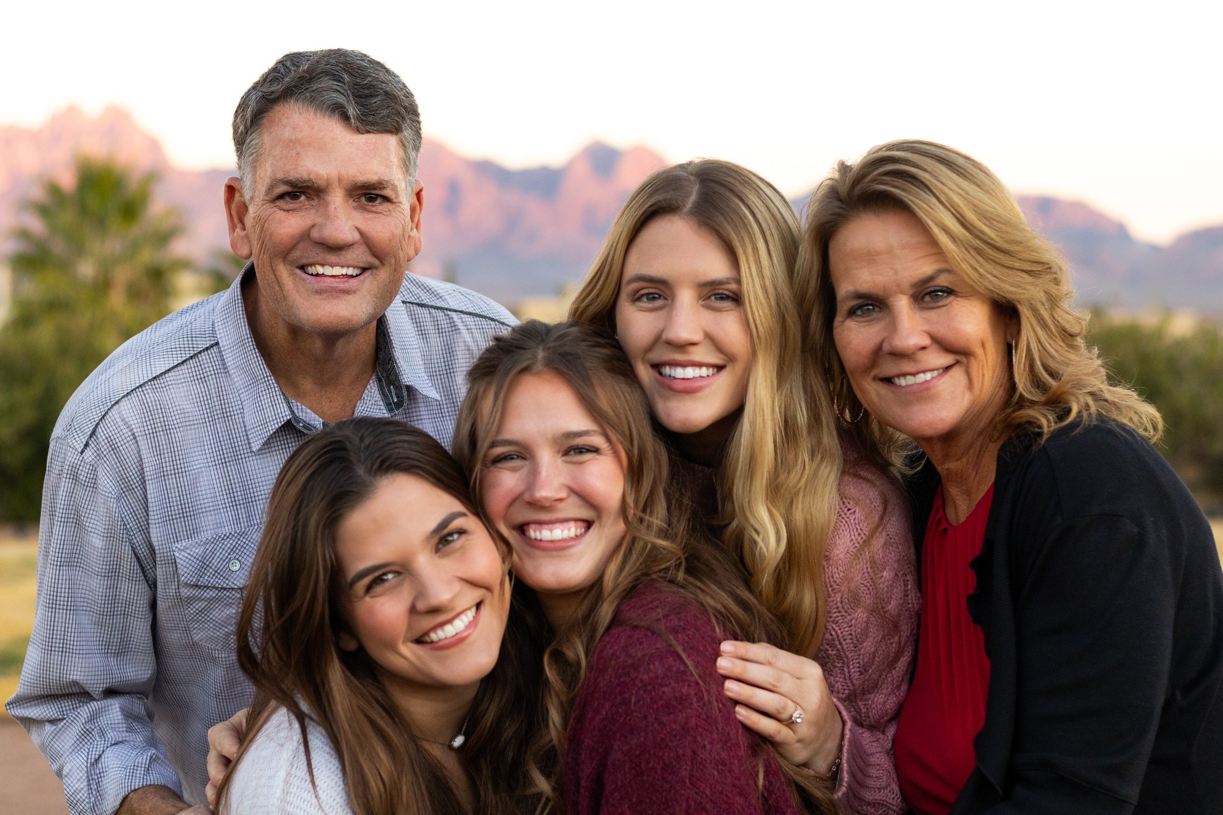 Family of six smiling outdoors with mountains in the background.
