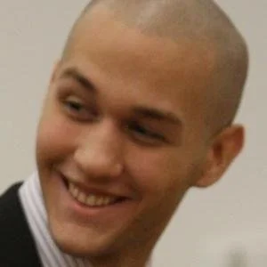 Close-up of a smiling man with a shaved head, wearing a striped shirt.