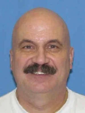 Close-up of a smiling bald man with a mustache against a blue background.